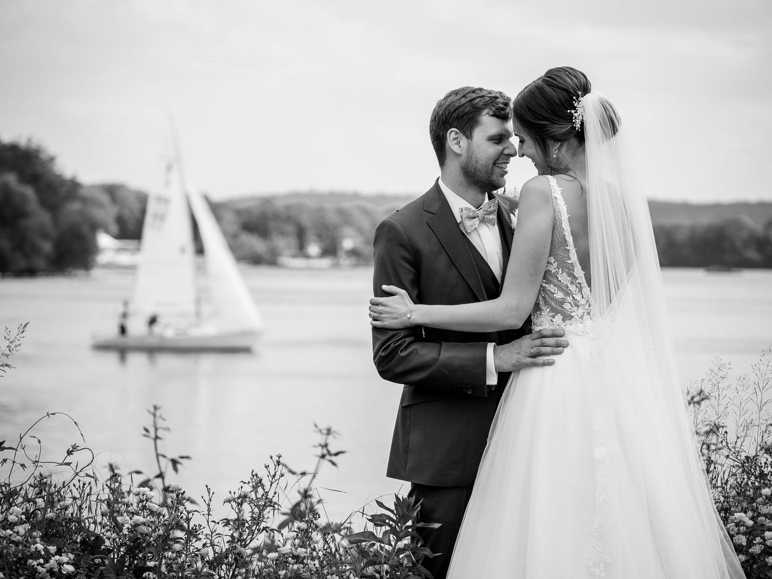 Black and white wedding photography captures romantic moments by a serene waterfront setting.
