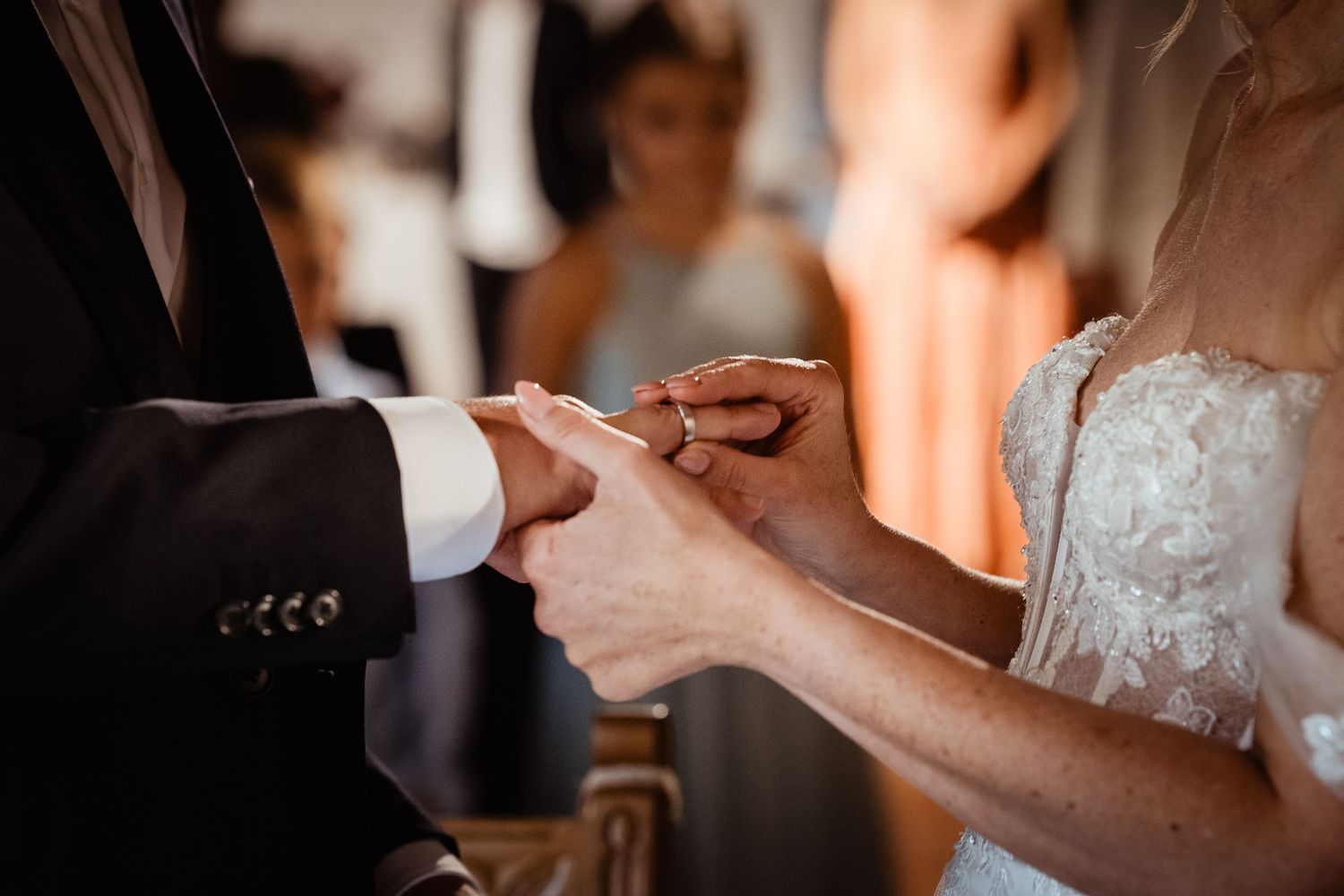 Bride placing a wedding ring on groom's finger during an elegant wedding ceremony.