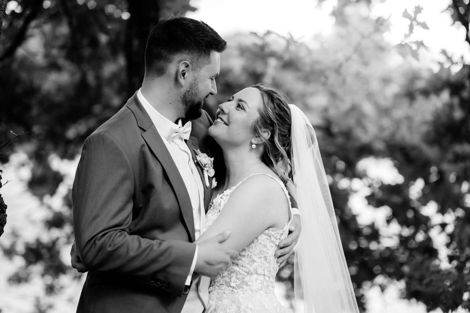 Black and white photo of a bride and groom sharing an intimate moment outdoors, surrounded by lush trees on their wedding day.