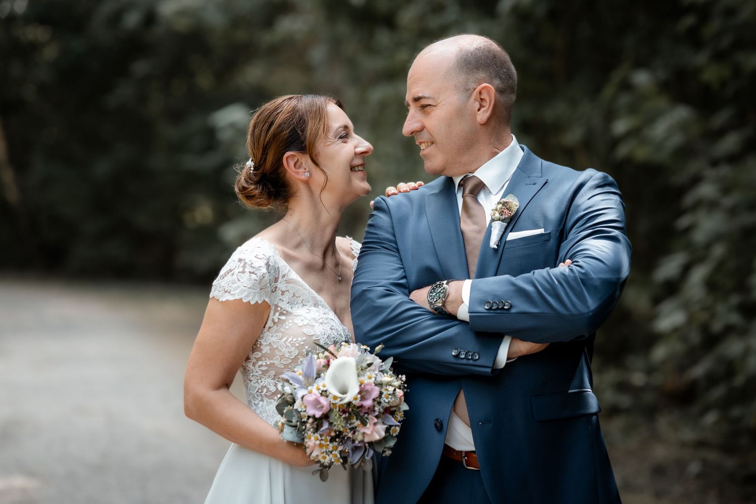 Happy bride and groom sharing a joyful moment outdoors, bride holding a pastel bouquet.