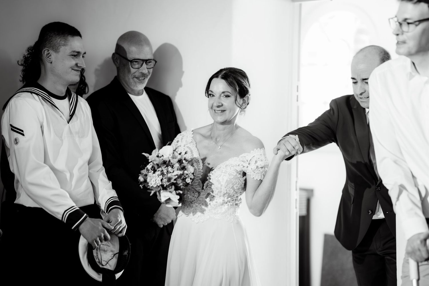 Black and white photo of bride holding bouquet, smiling with wedding guests during ceremony greeting.