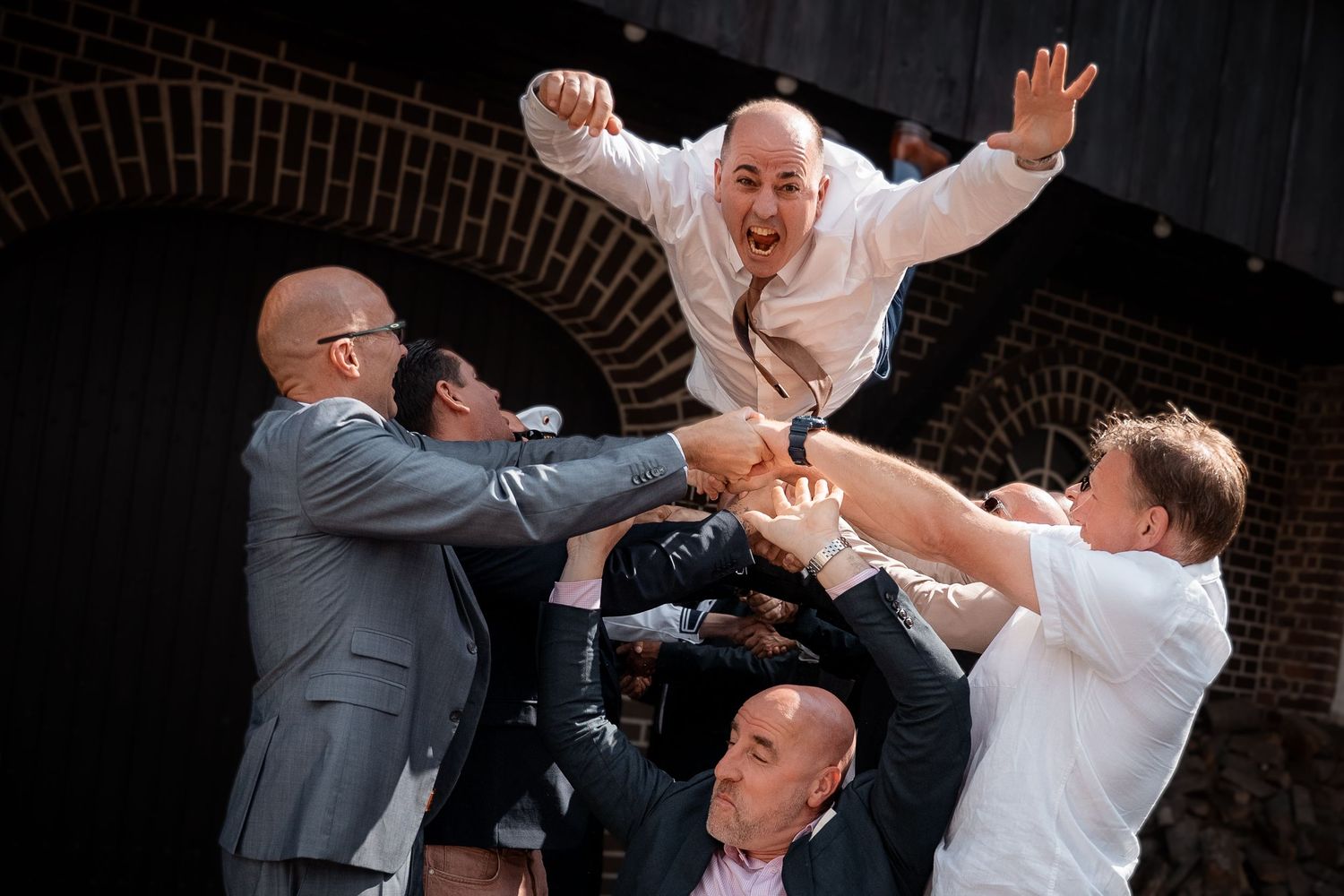 Groomsmen joyfully toss the groom into the air during a lively wedding celebration.