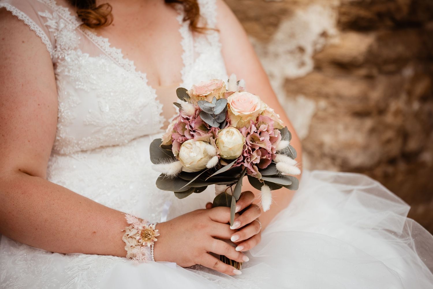 Close-up of bride holding a romantic bouquet of roses and hydrangeas in soft pink and cream tones.