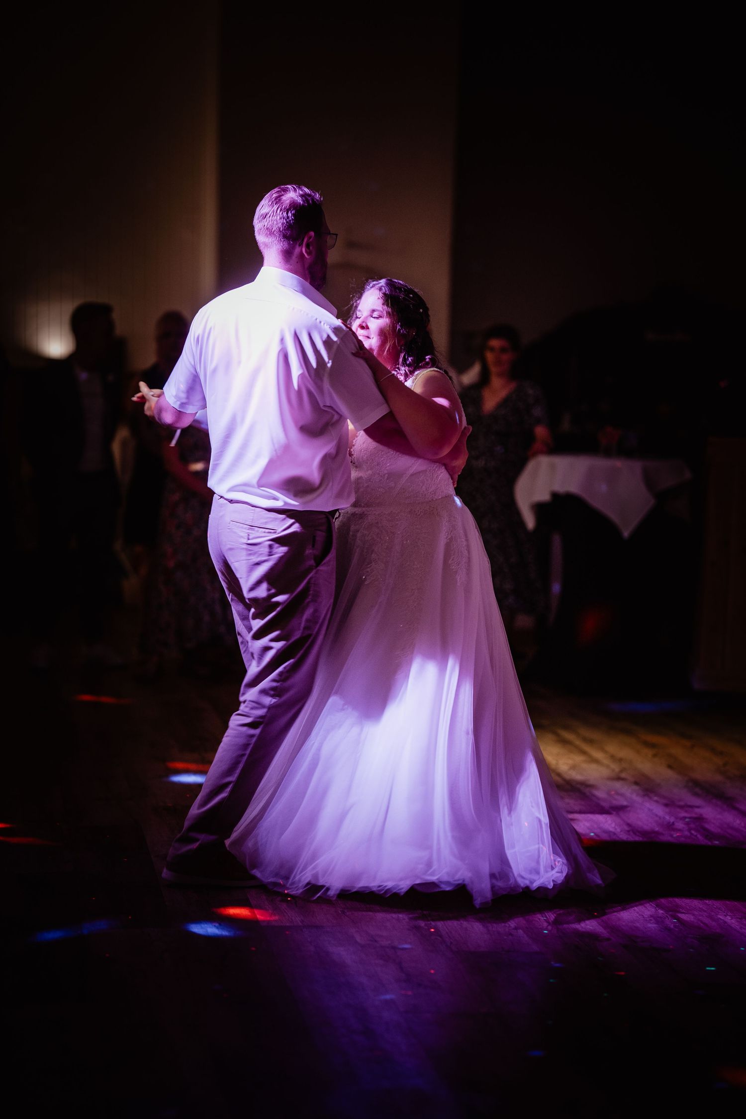 Bride and groom share romantic first dance bathed in purple spotlight at evening wedding reception.
