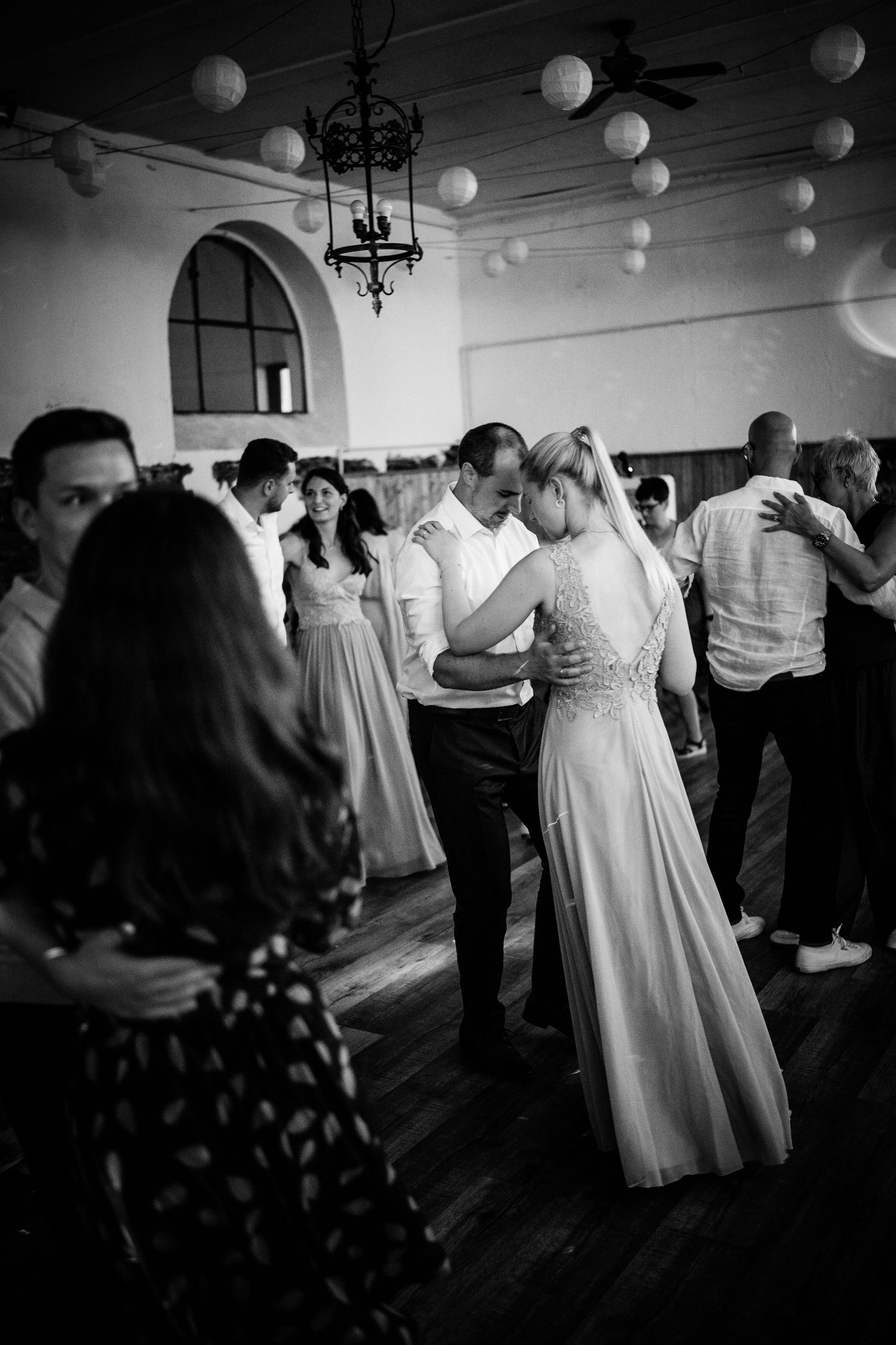 Couples dance together at wedding reception in decorated hall with globe lights in black and white.