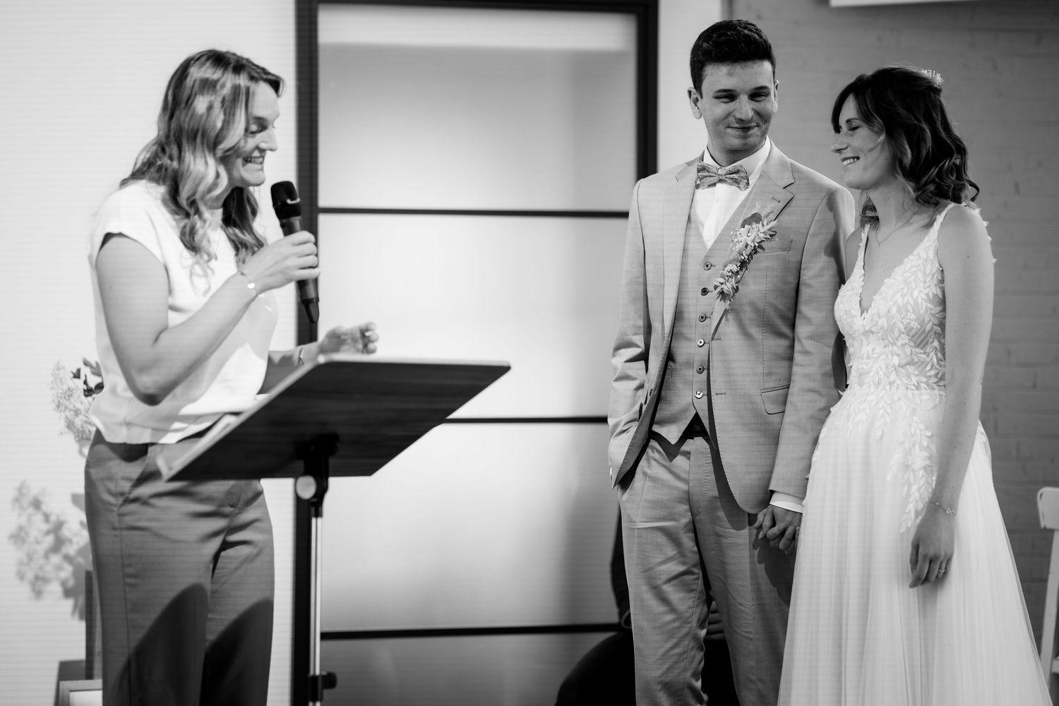 Black and white photo of smiling officiant speaking to happy bride and groom during wedding ceremony.