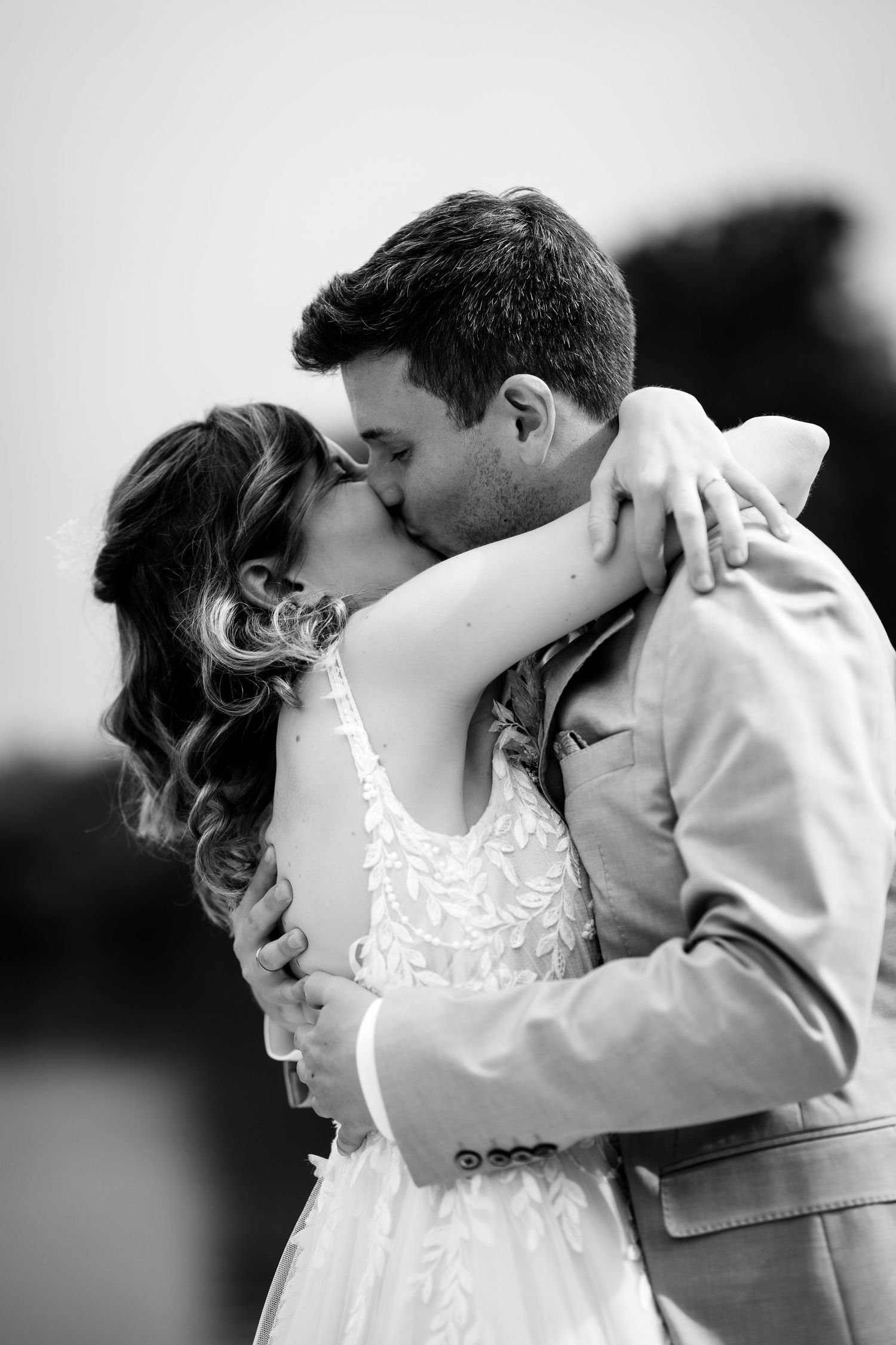 A bride and groom share a romantic kiss outdoors in a black and white wedding portrait.