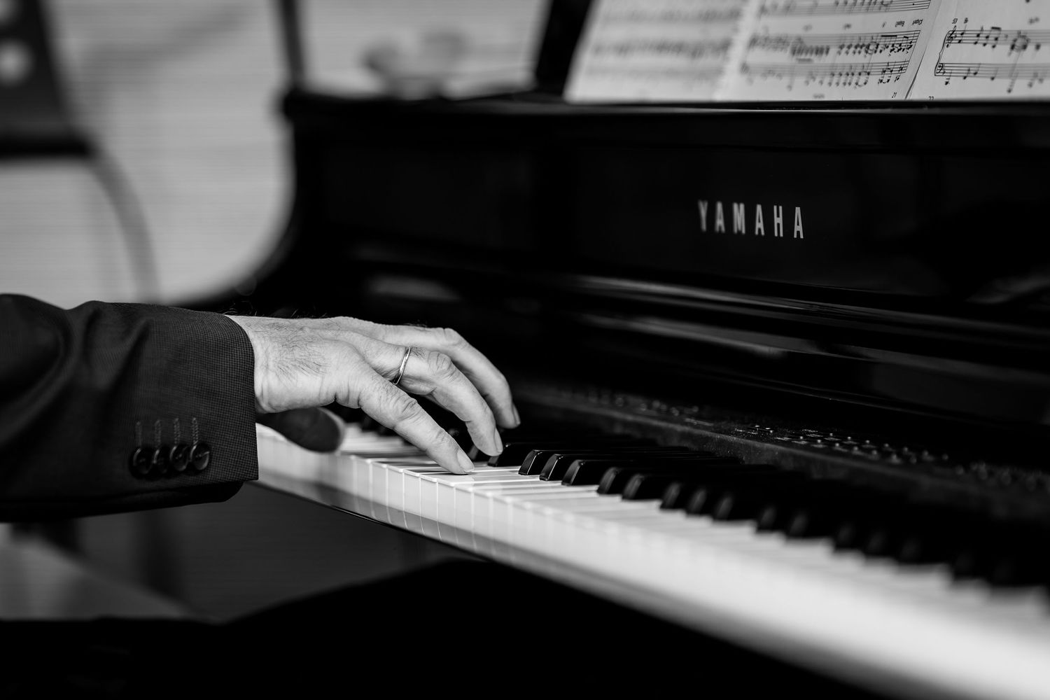 Close-up of hands playing Yamaha grand piano keys in black and white photography.