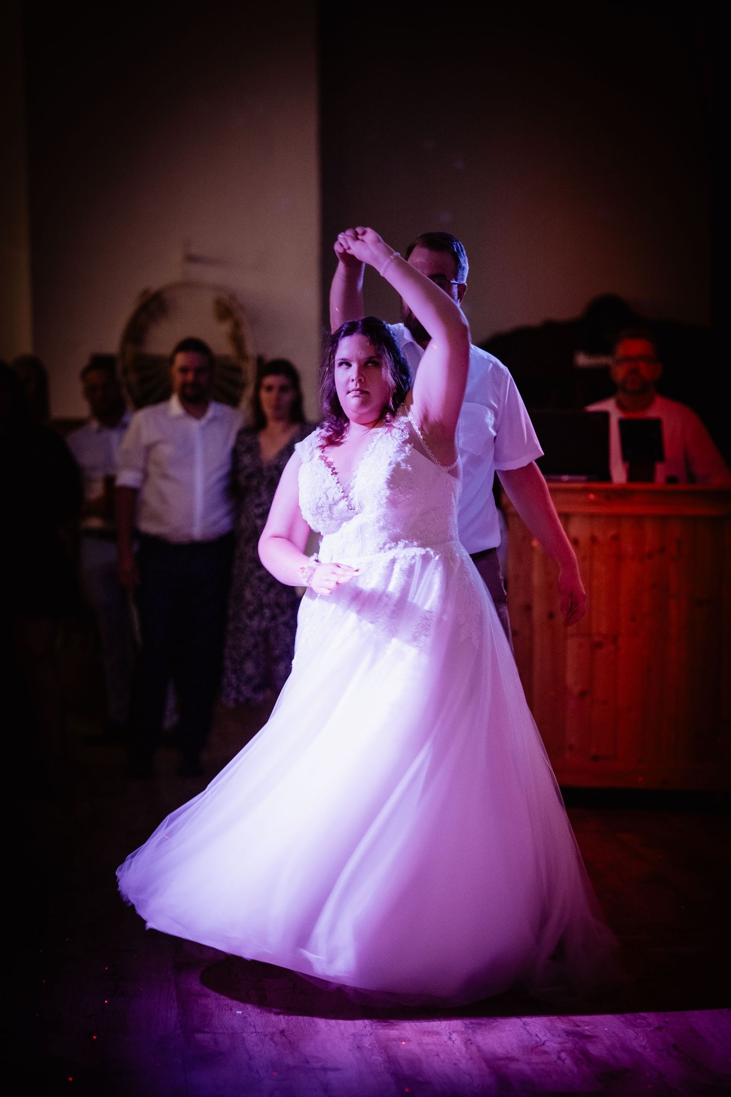Bride in white ball gown twirling during first dance under purple wedding reception lights.