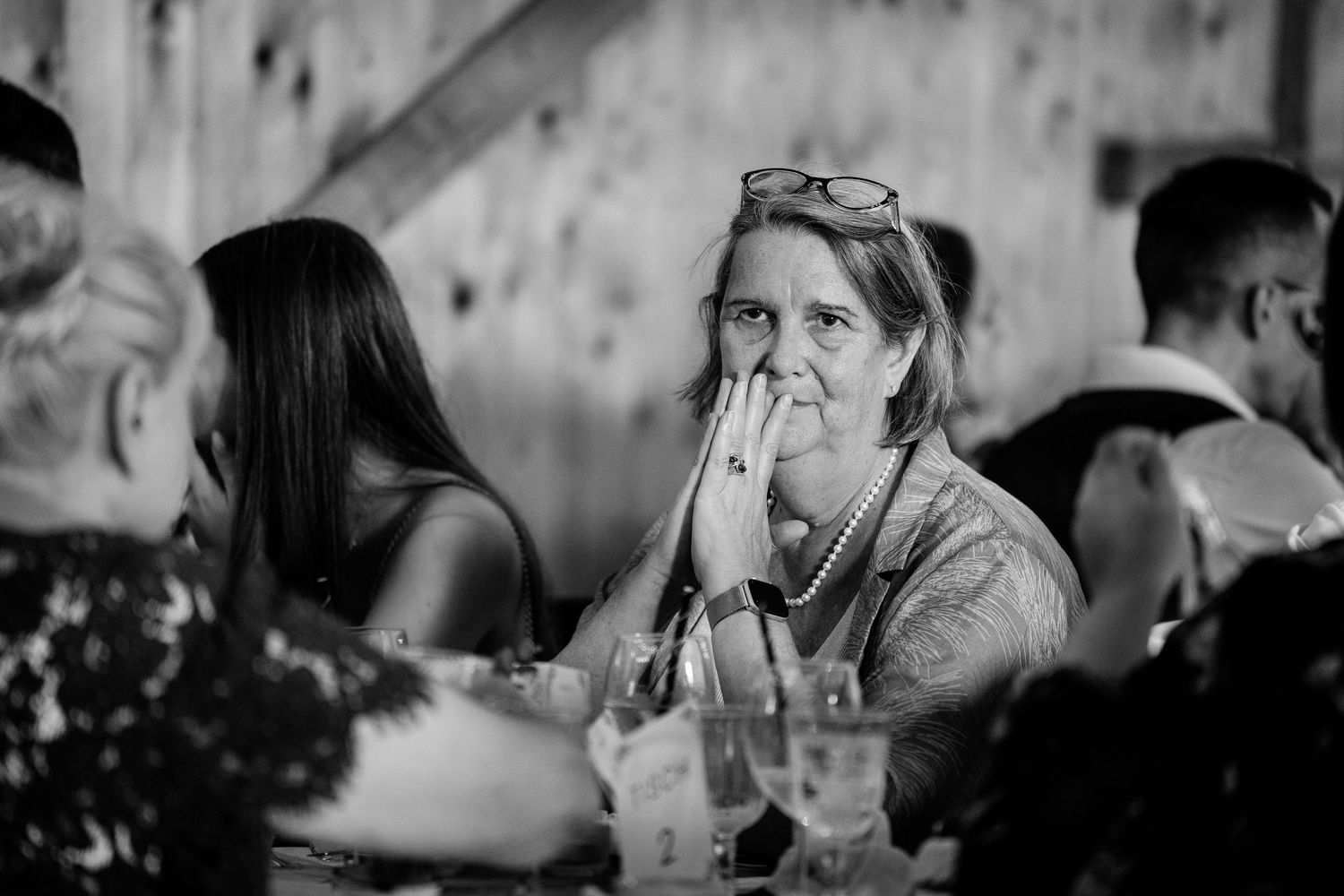 Emotional wedding guest with hand over mouth seated at reception table in candid black and white photo.