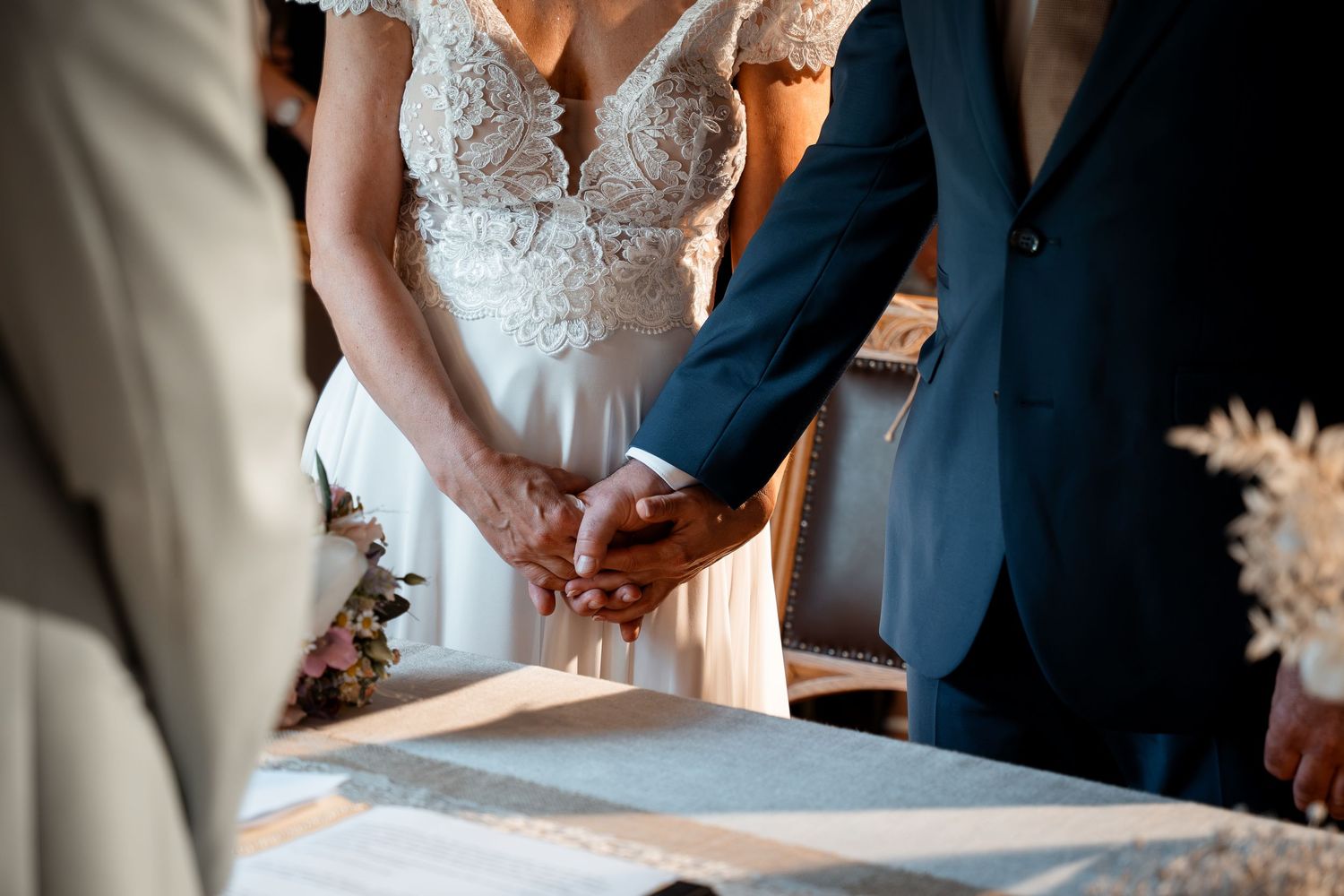 Bride and groom hold hands at the altar during their wedding ceremony beside a document-covered table.