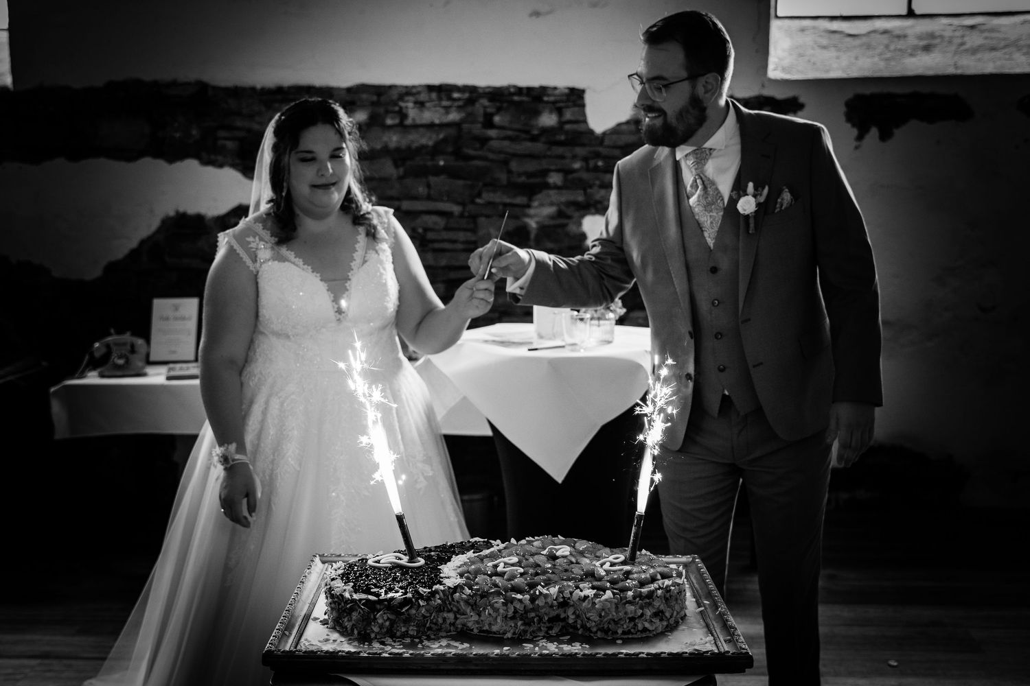 Black and white photo of bride and groom cutting wedding cake with sparklers.