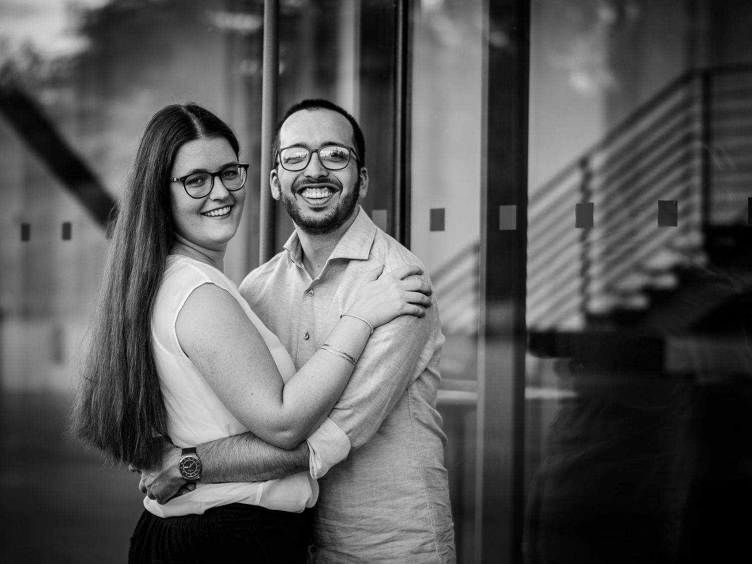 Black and white photo of smiling couple embracing outside a modern building.