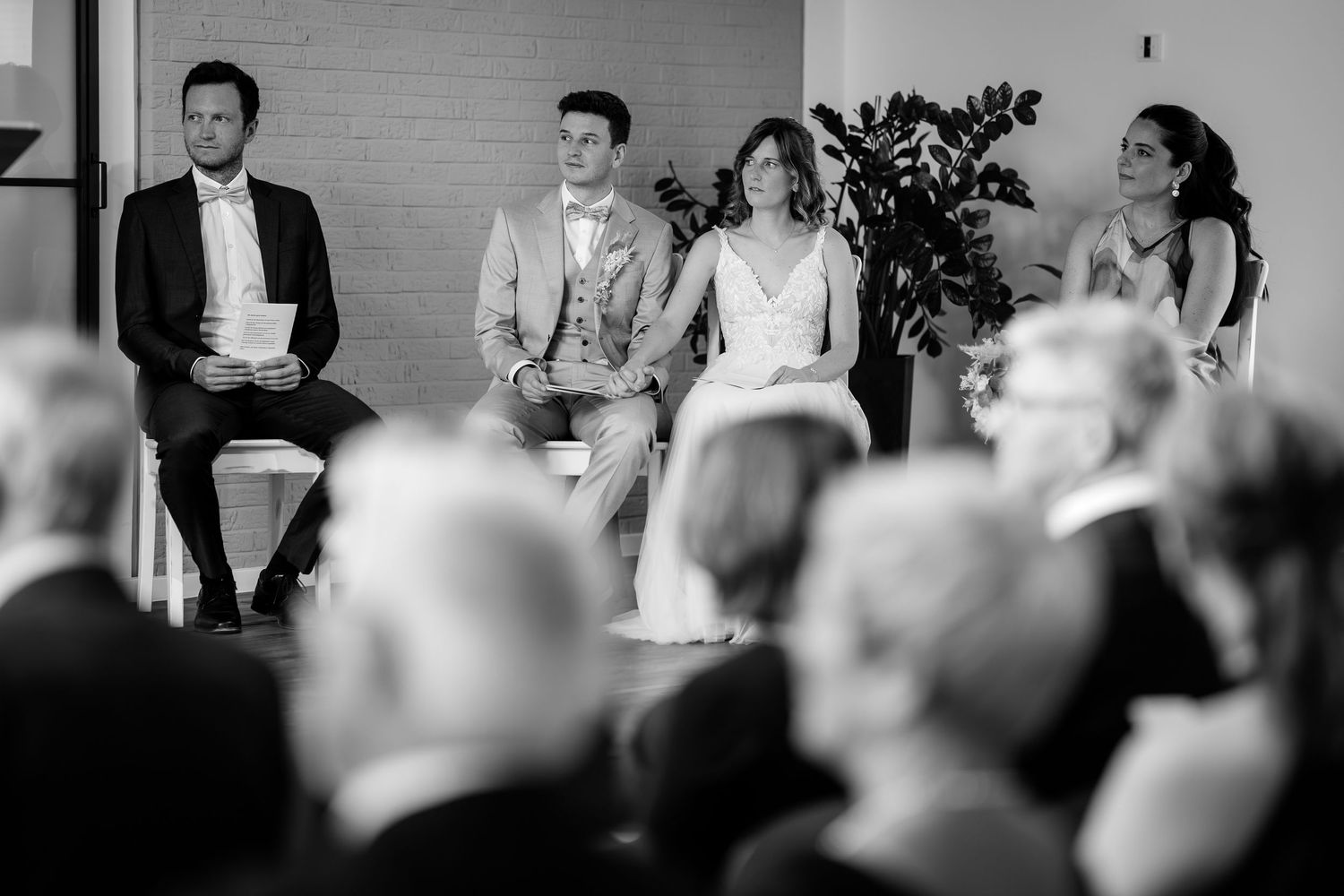 Black and white wedding ceremony photo of bride, groom, and guests seated in a modern venue.