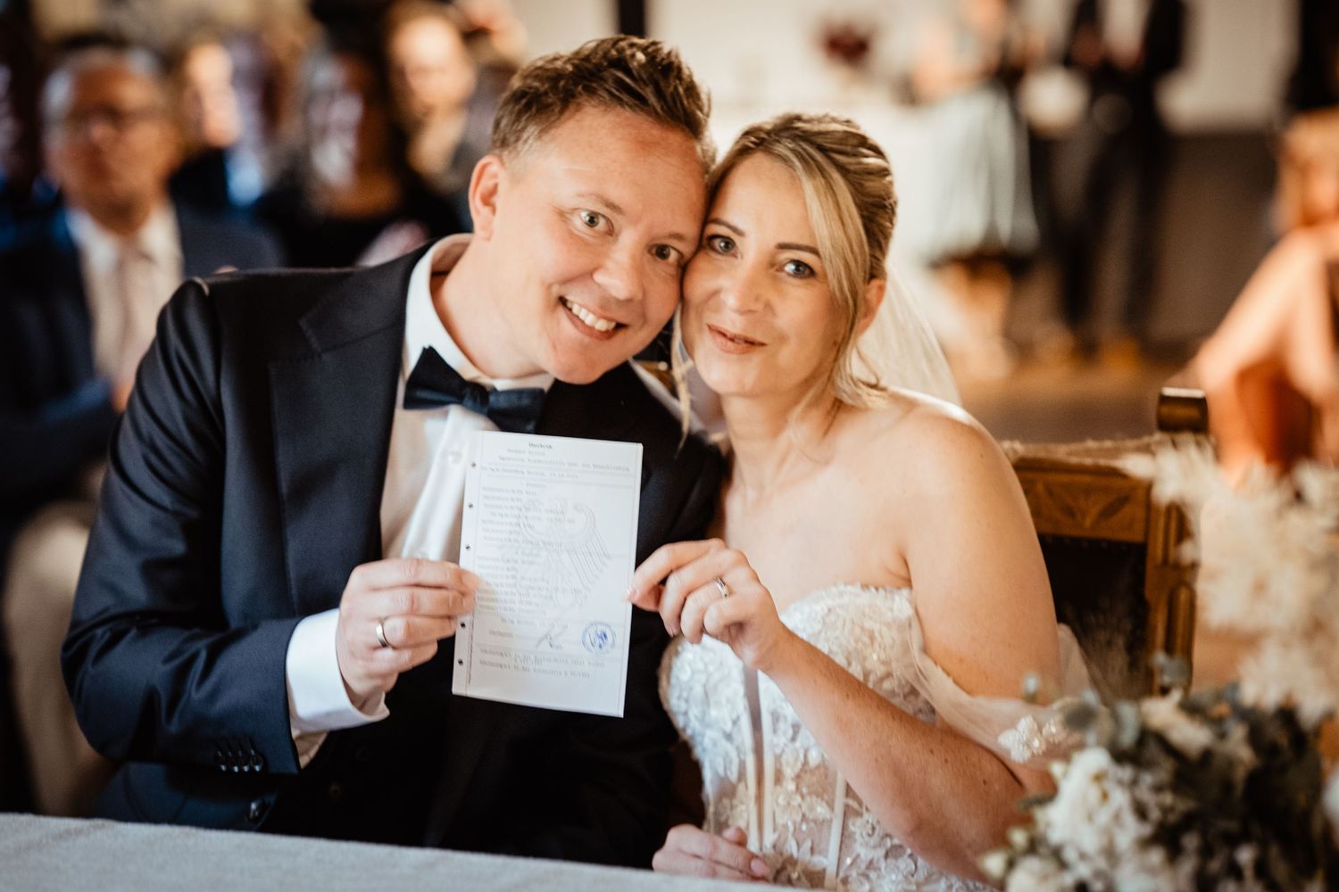 Smiling newlyweds proudly displaying their marriage certificate at wedding reception.