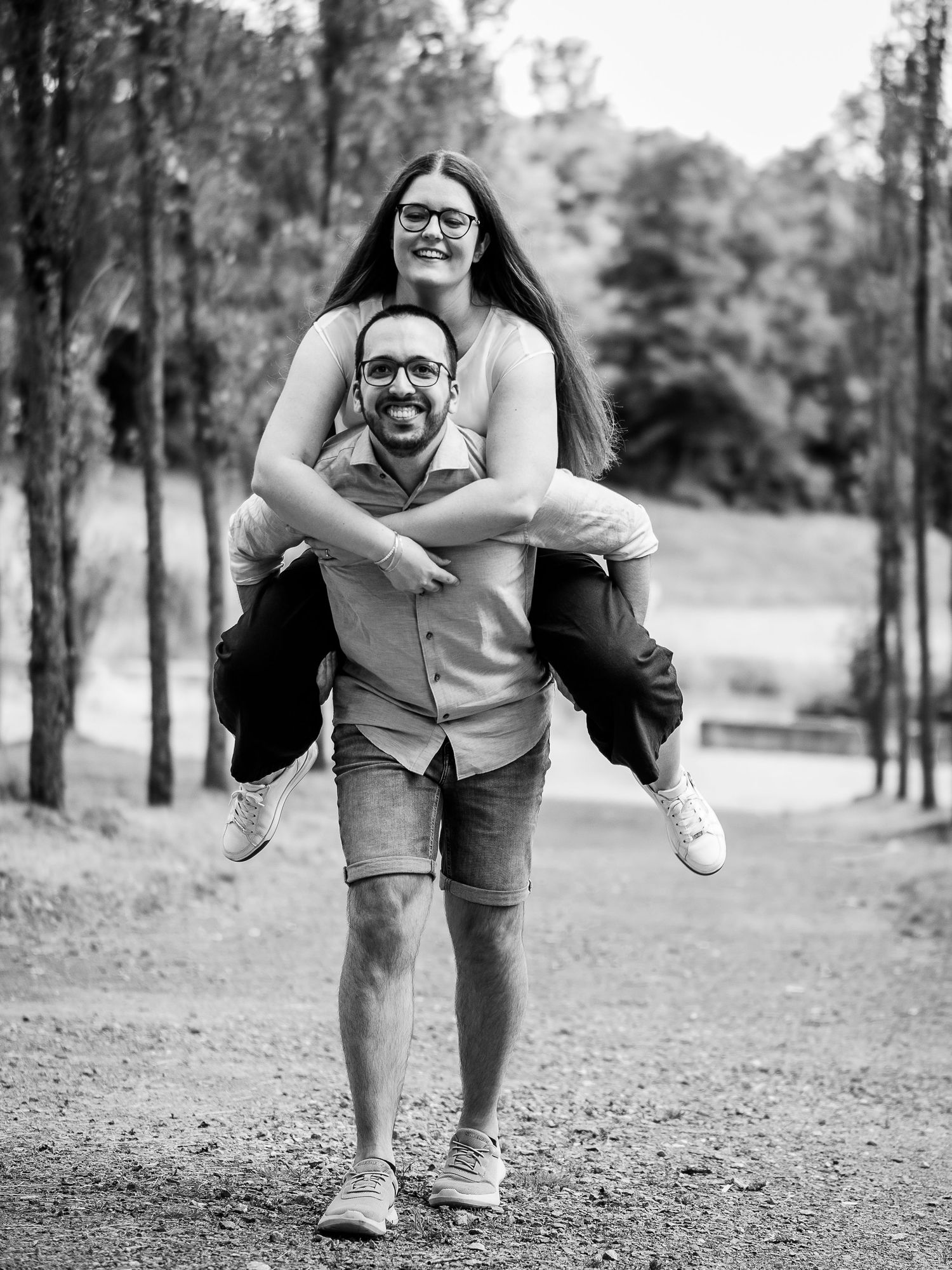 Man giving woman a piggyback ride along a scenic park path in a fun black and white couple portrait.