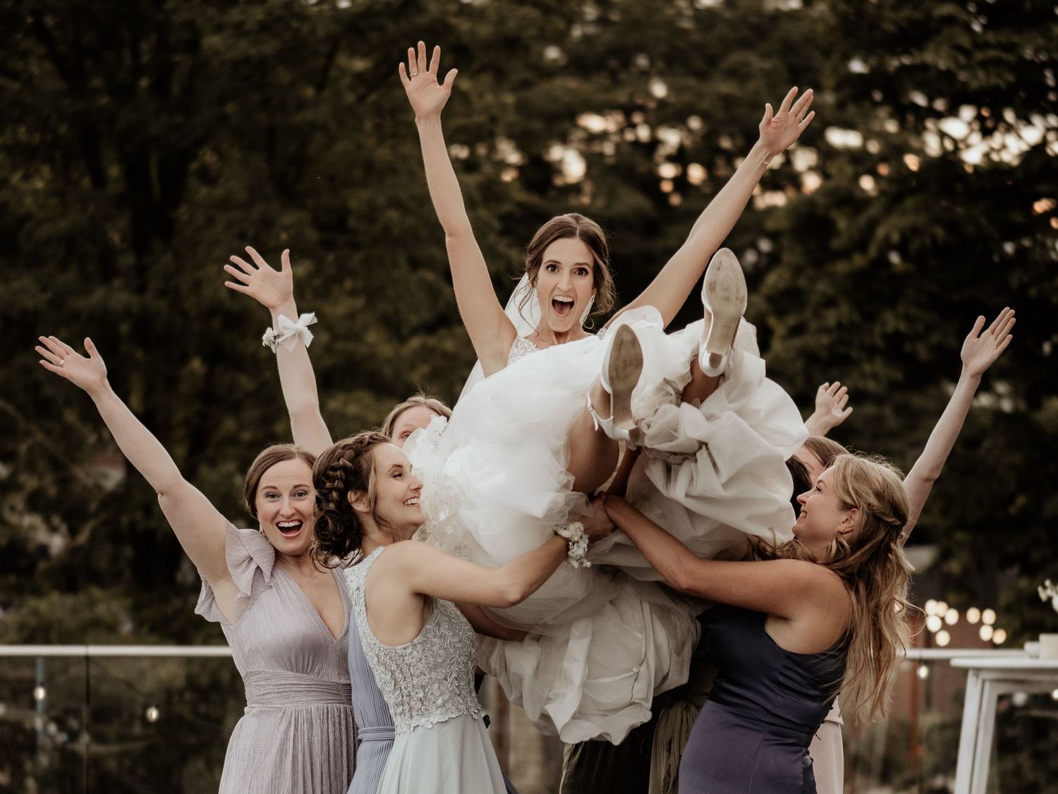 Wedding party celebrates joyfully with raised arms outdoors in matching dresses during golden hour.