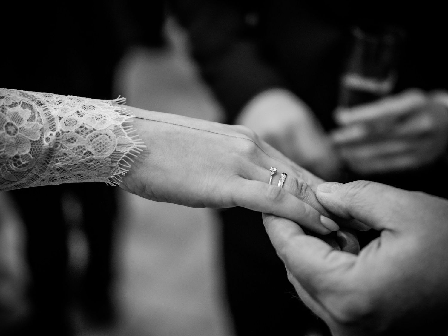 Close-up black and white photo of wedding ring on brides finger with lace sleeve detail.