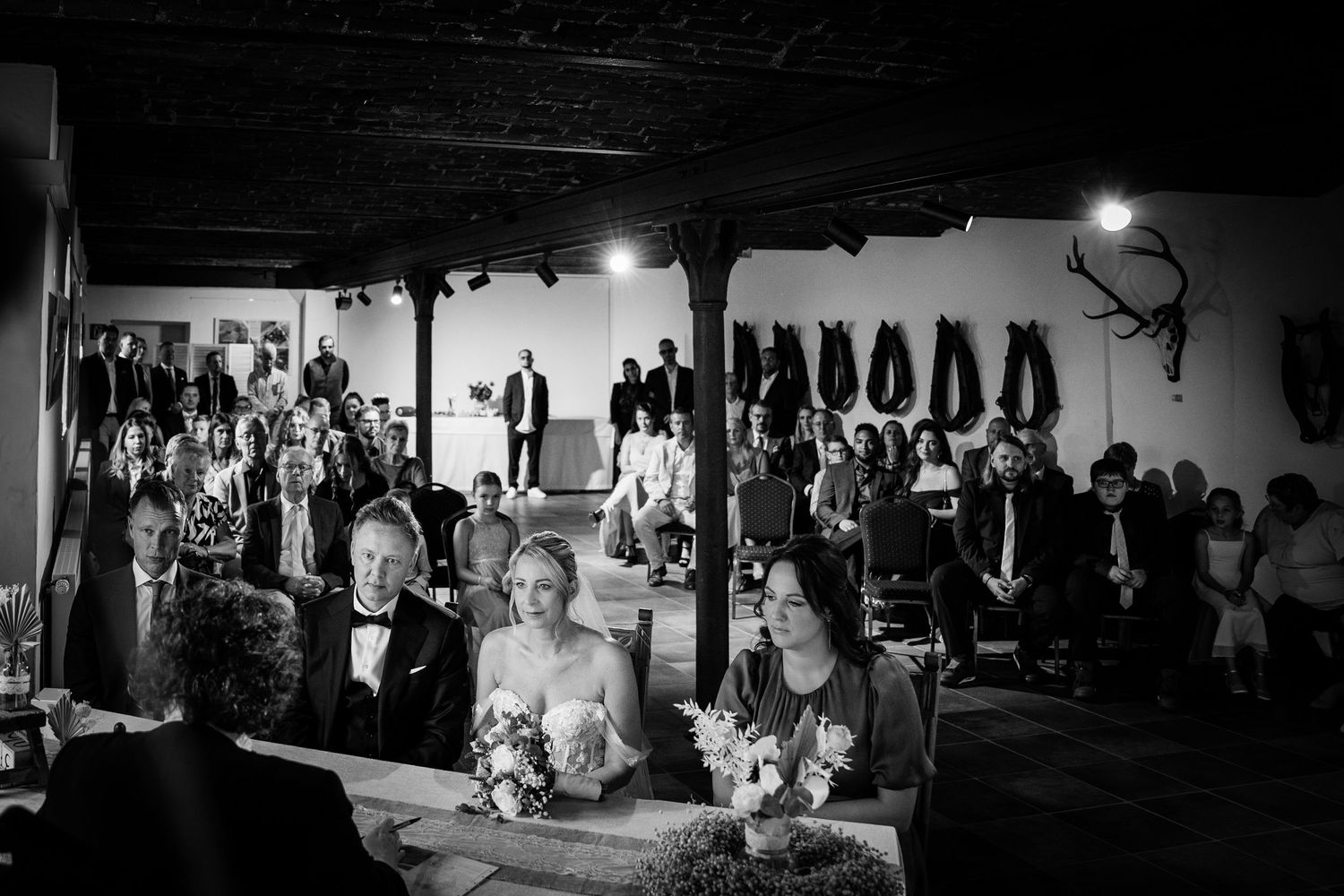 Wedding ceremony in a rustic barn venue with guests seated as bride walks down the aisle.