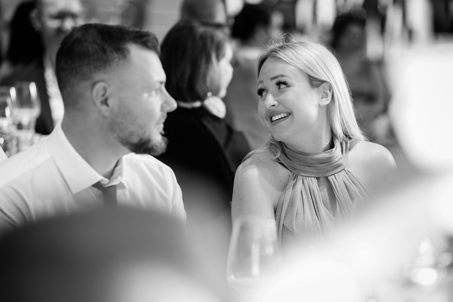 Black and white candid photo of smiling wedding guests conversing at reception table.