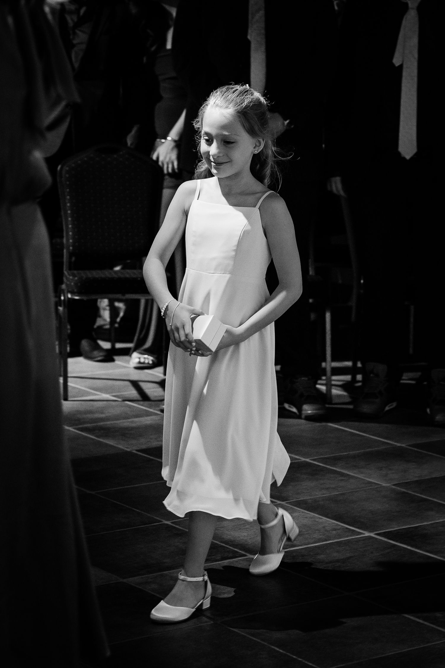 Young flower girl in white dress smiling at wedding reception in black and white.