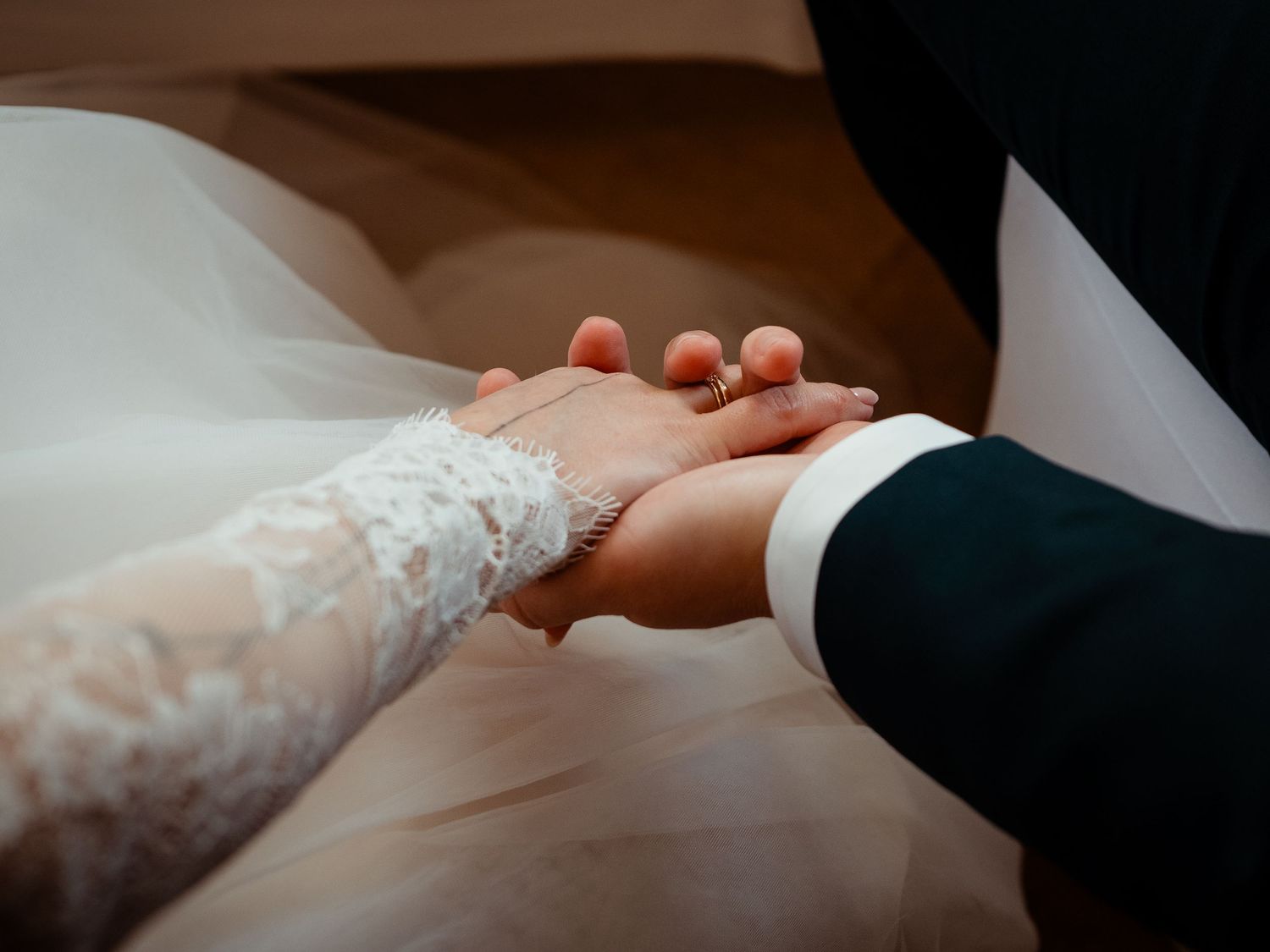 Bride and groom hold hands tenderly, showcasing lace wedding dress sleeve and engagement ring.