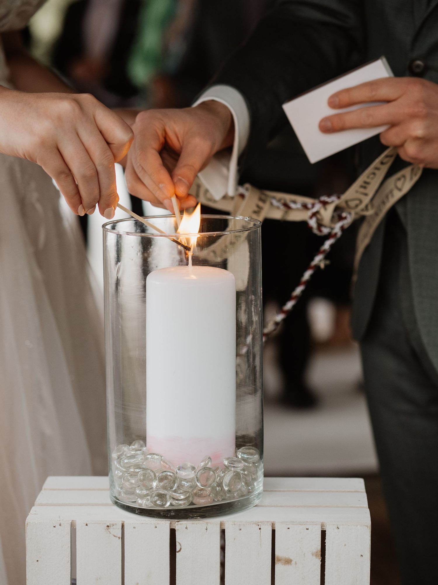 Couple lighting a unity candle in a glass vase during a wedding ceremony.
