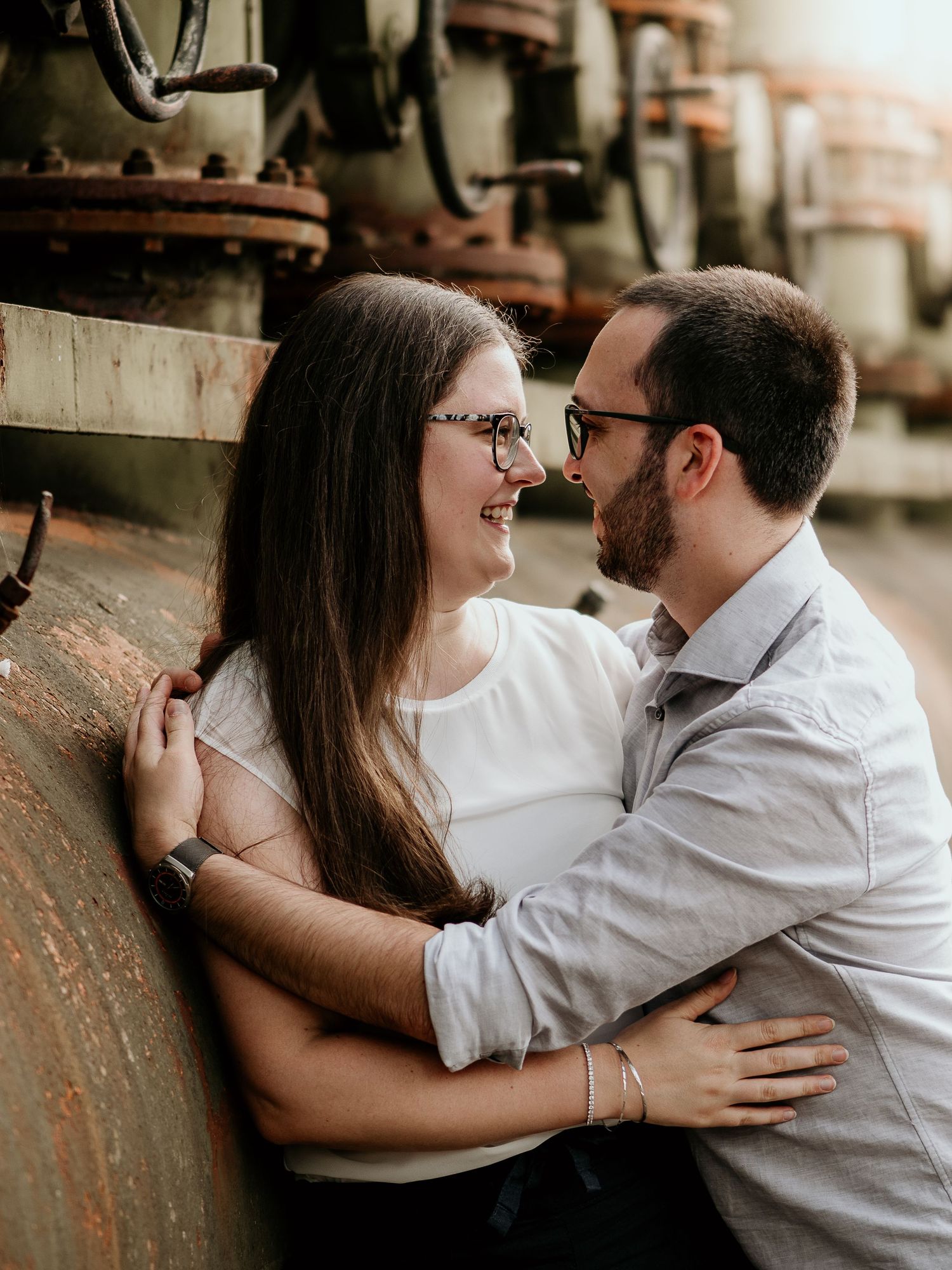 A couple shares an intimate moment against a rustic brick wall in a romantic engagement photoshoot series.