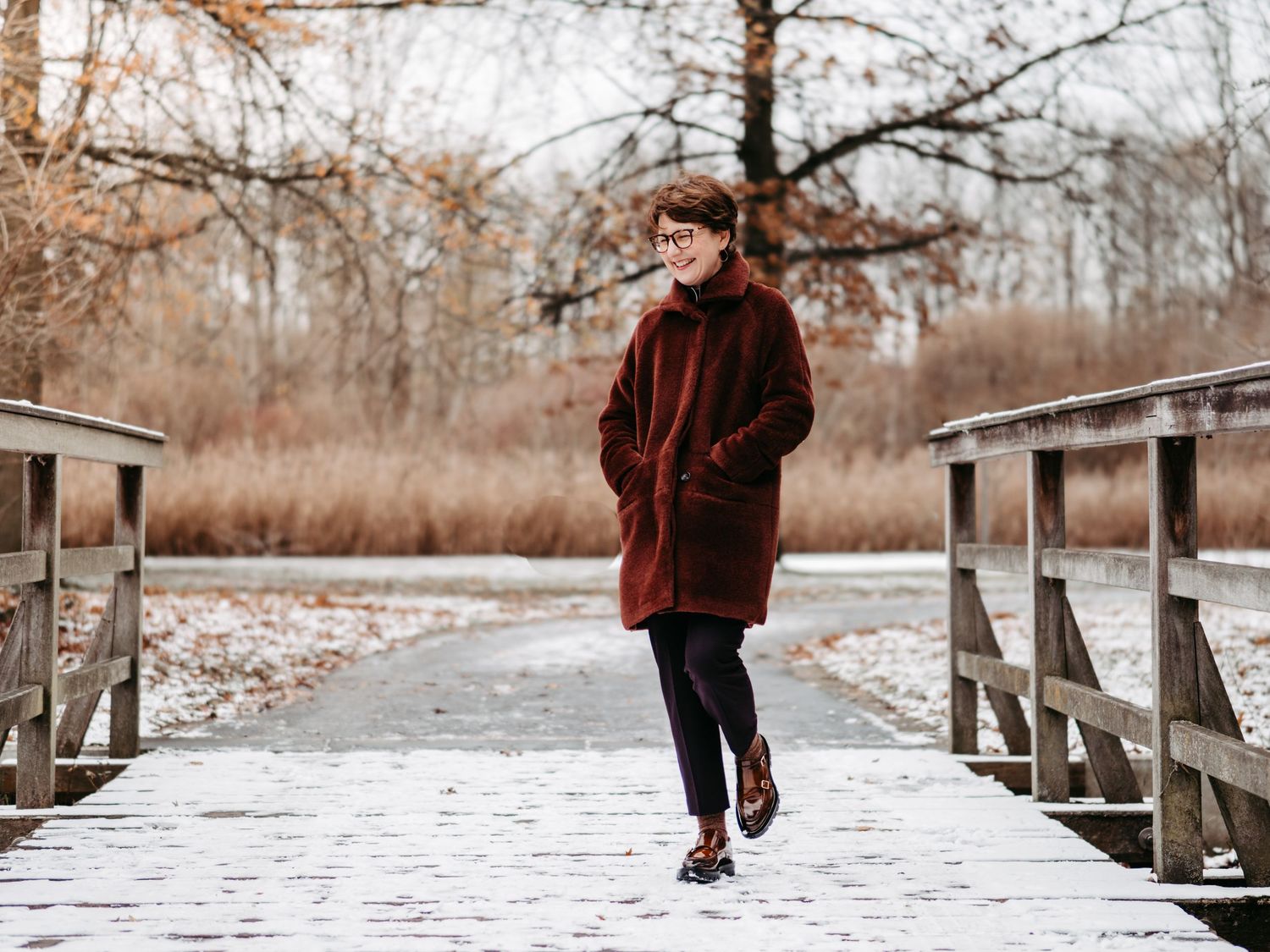 A person walks along a snowy wooden boardwalk through a winter landscape in warm earth tones.