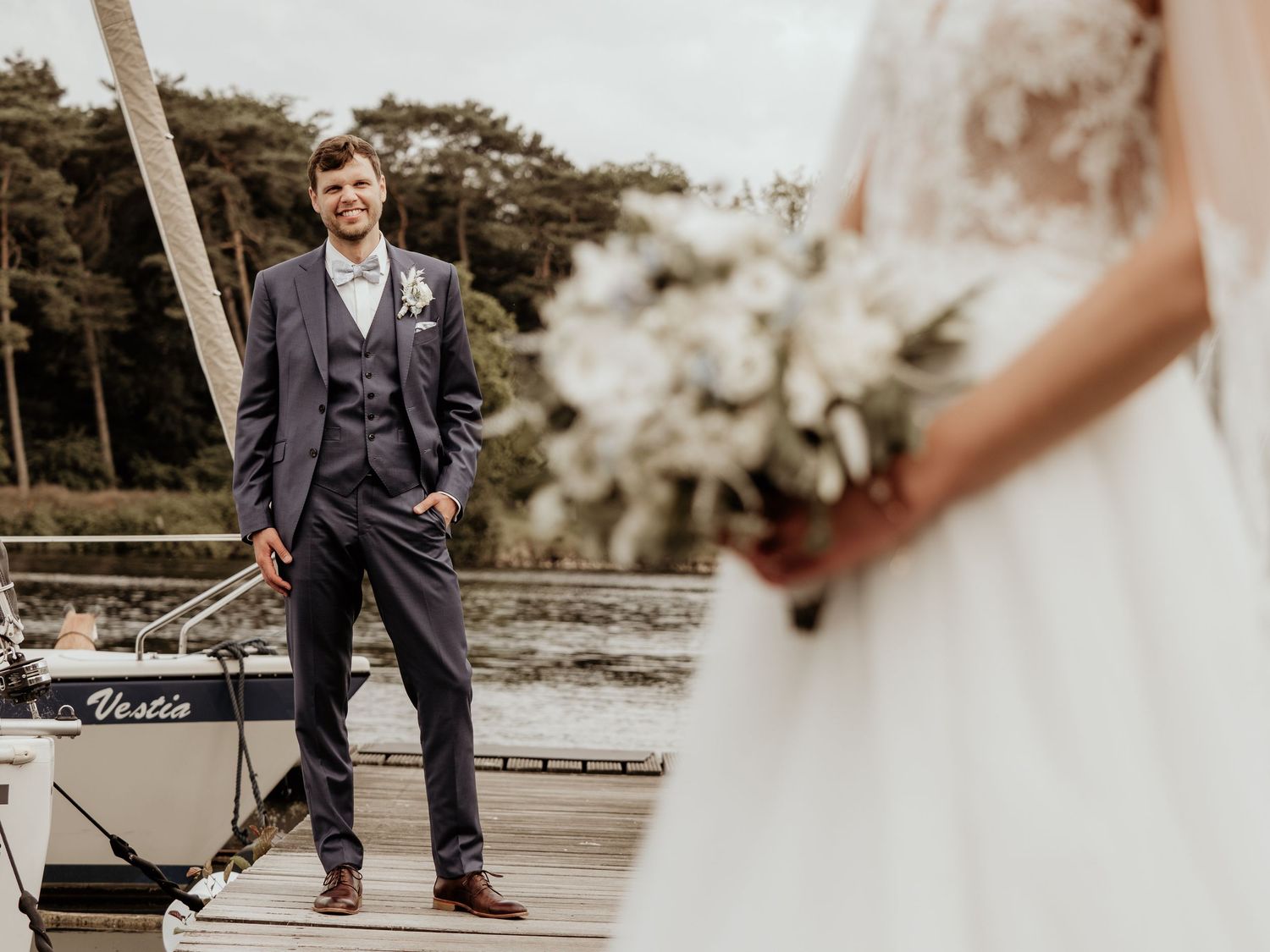 Wedding couple shares intimate moments on a lakeside dock with sailboats in the background.