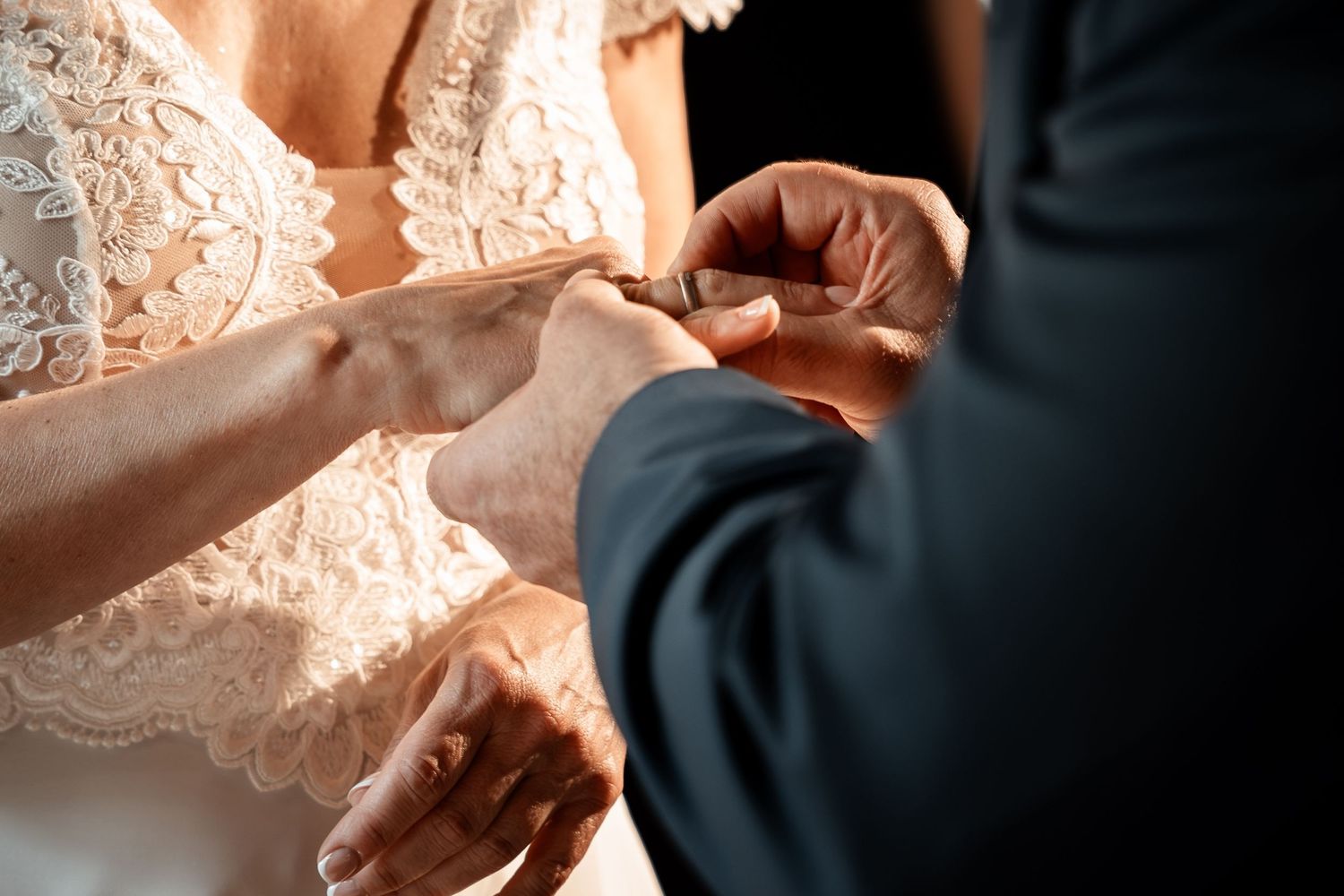 Close-up of groom placing wedding ring on bride's finger during ring exchange ceremony.