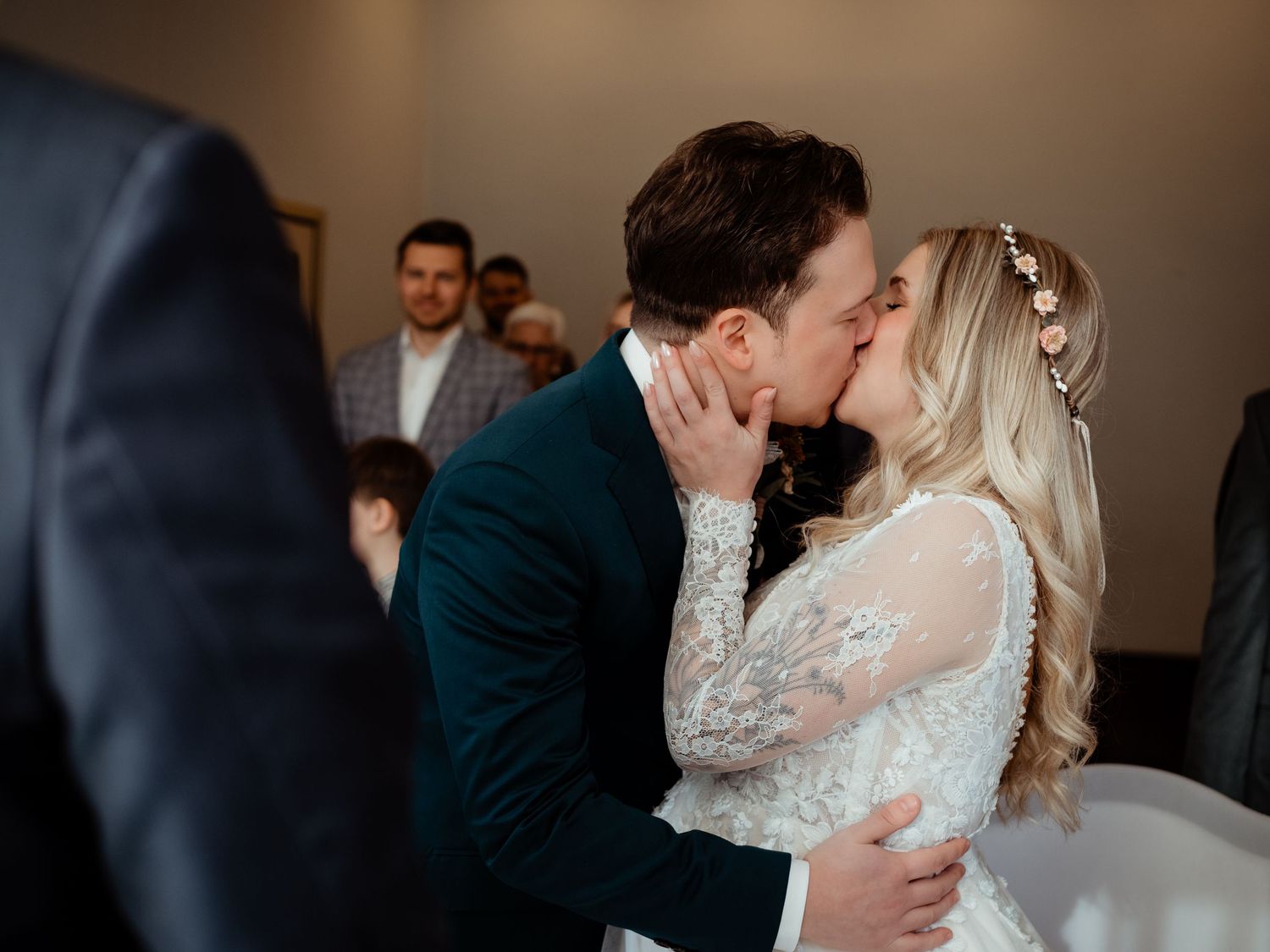 Bride and groom share their first kiss at the wedding altar, surrounded by guests.