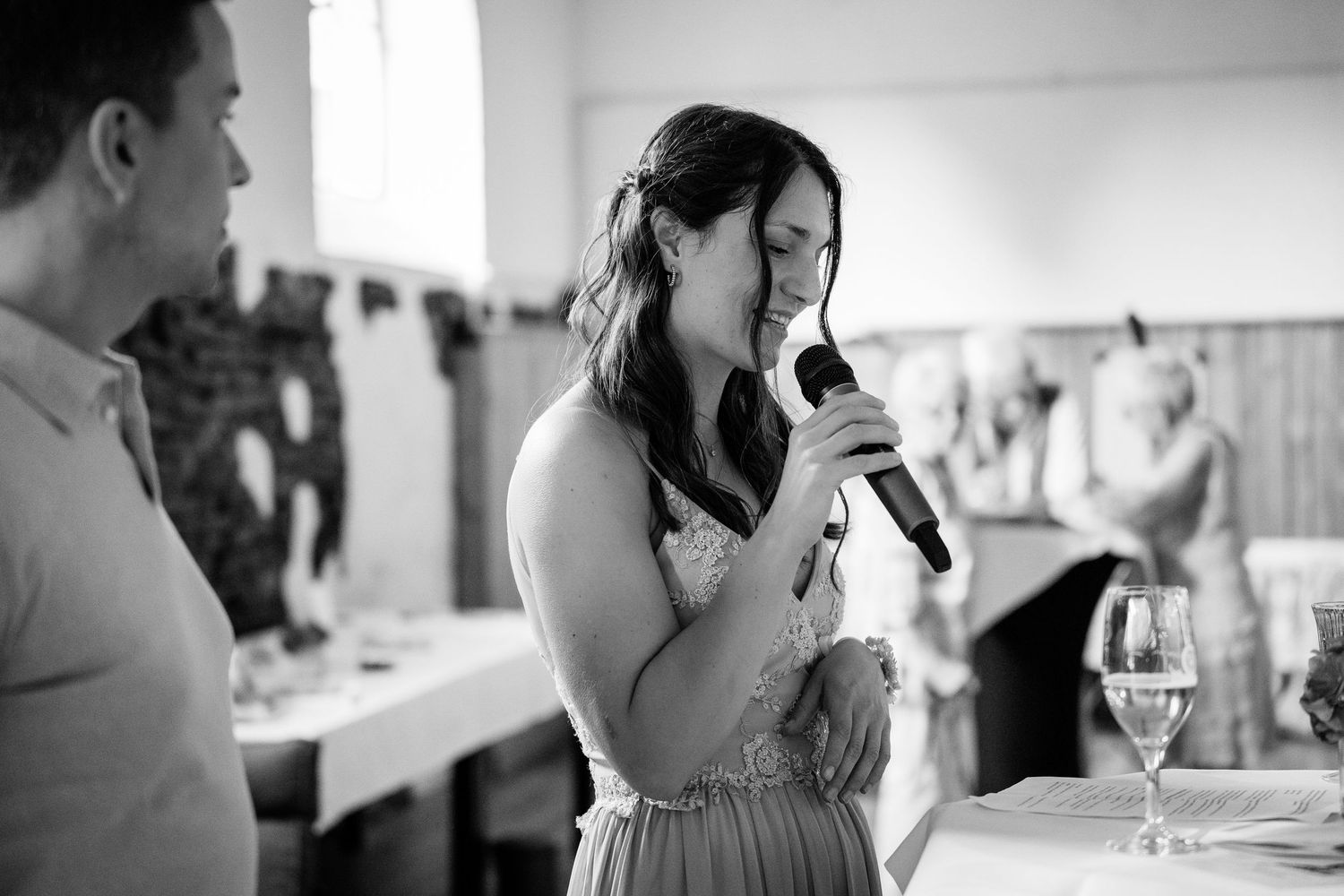 Bridesmaid speaking into microphone during wedding reception speech in black and white.
