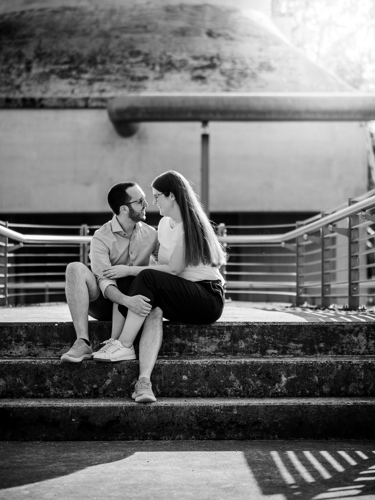 Black and white photo of a couple sharing a romantic moment while sitting on outdoor steps with metal railings.