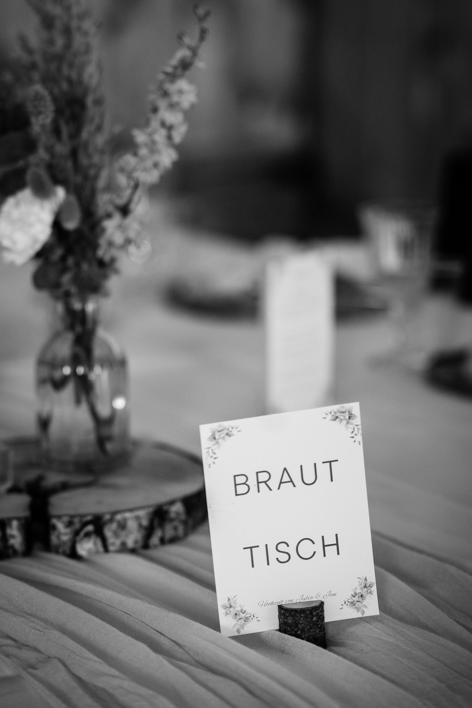Black and white photo of a Brauttisch wedding table sign in a wooden holder with floral centerpiece.
