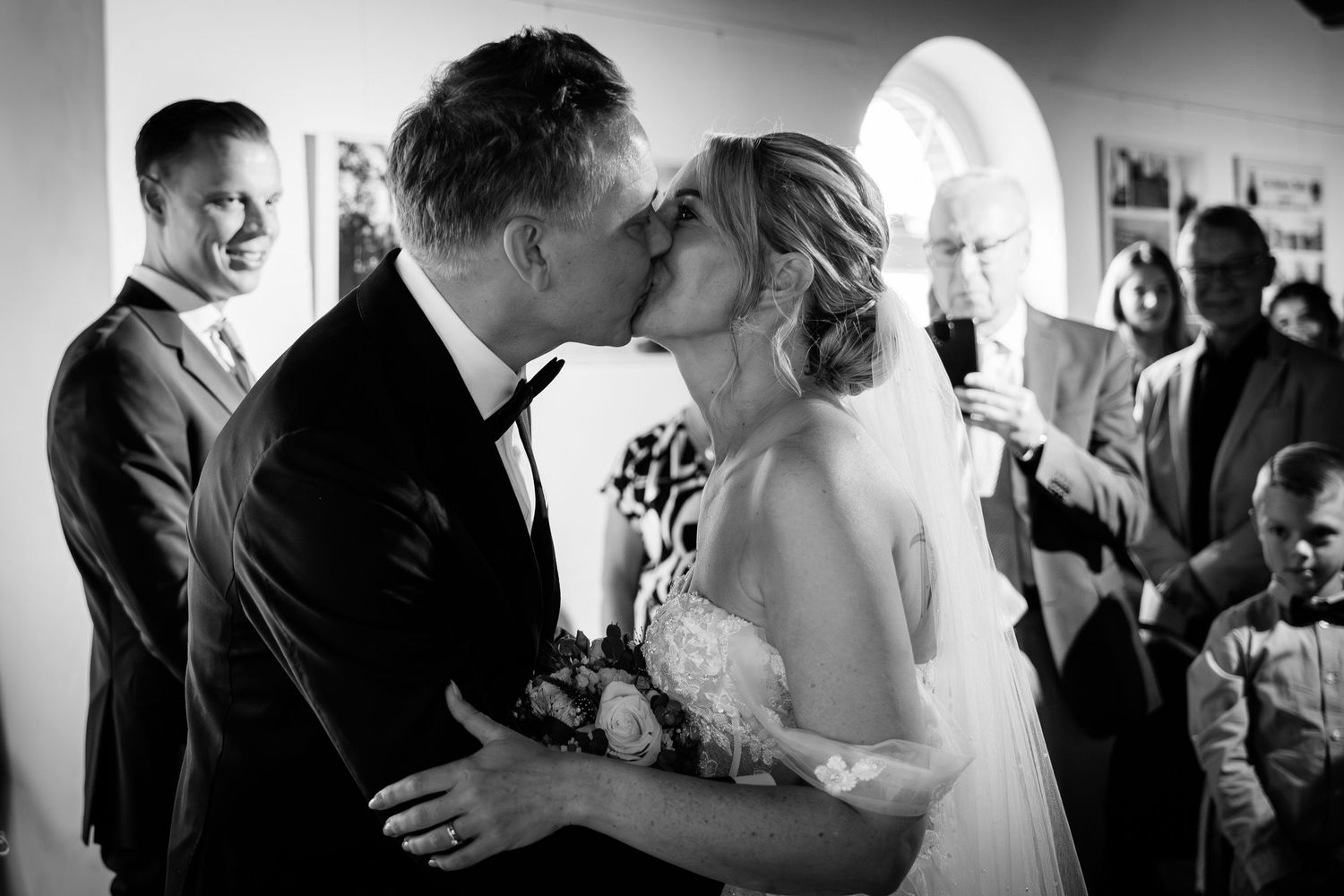 Black and white photo of a bride and groom sharing their first kiss at the wedding ceremony.