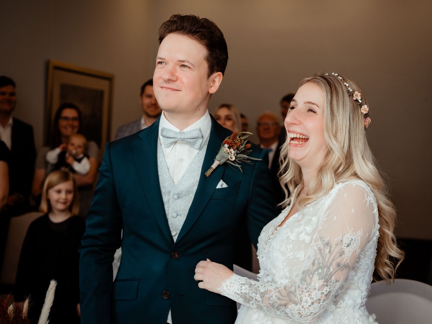 Joyful bride and groom laughing together during wedding ceremony, bride wearing lace gown and floral crown.