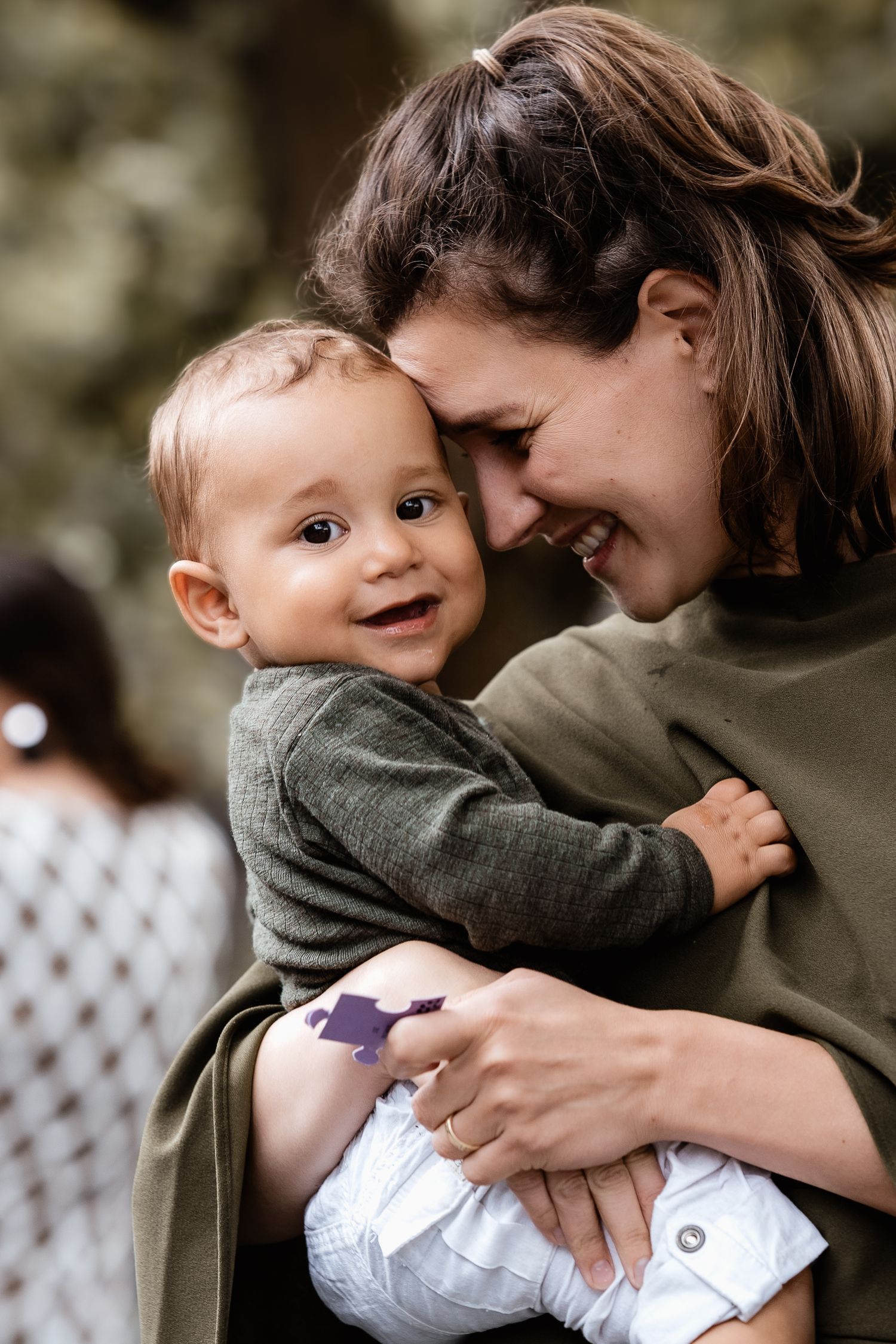 Smiling mother tenderly holds happy baby with foreheads touching outdoors.