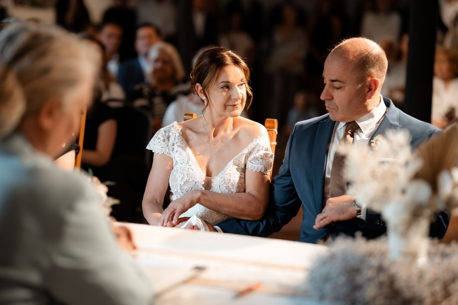 Bride and groom attentively listening during wedding ceremony, seated together at a decorated signing table.