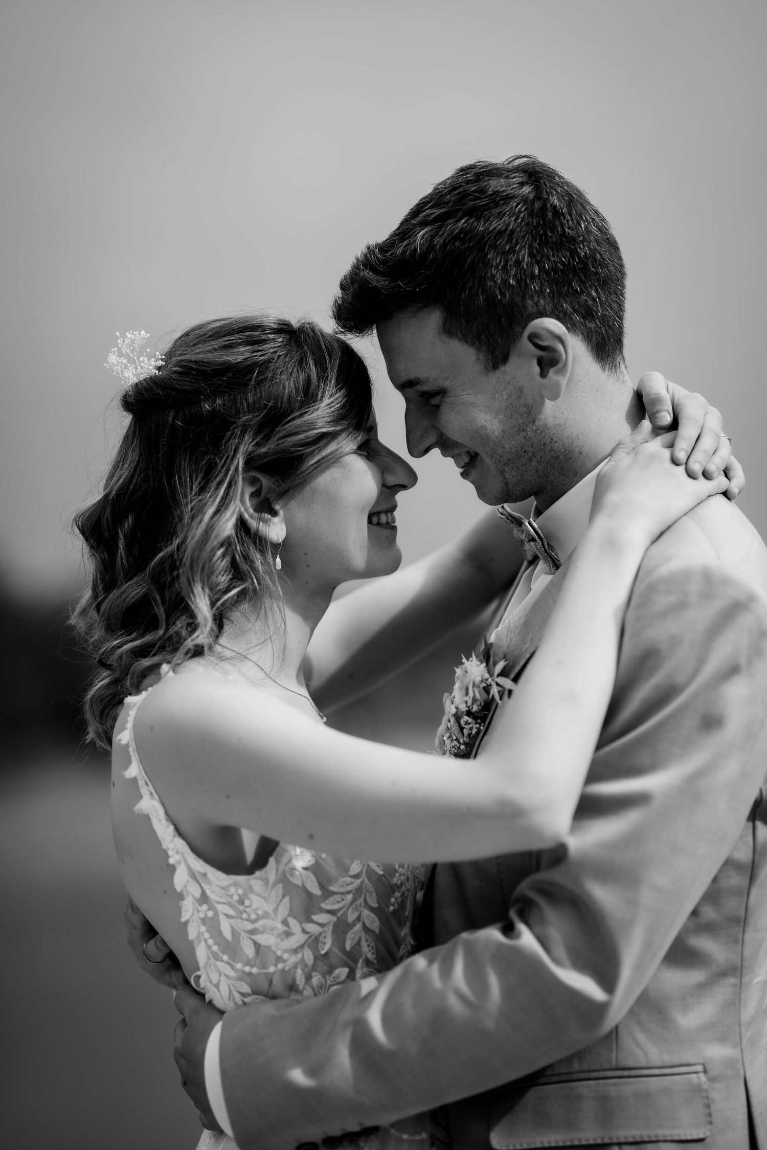 Black and white photo of a bride and groom embracing and smiling at each other on their wedding day.