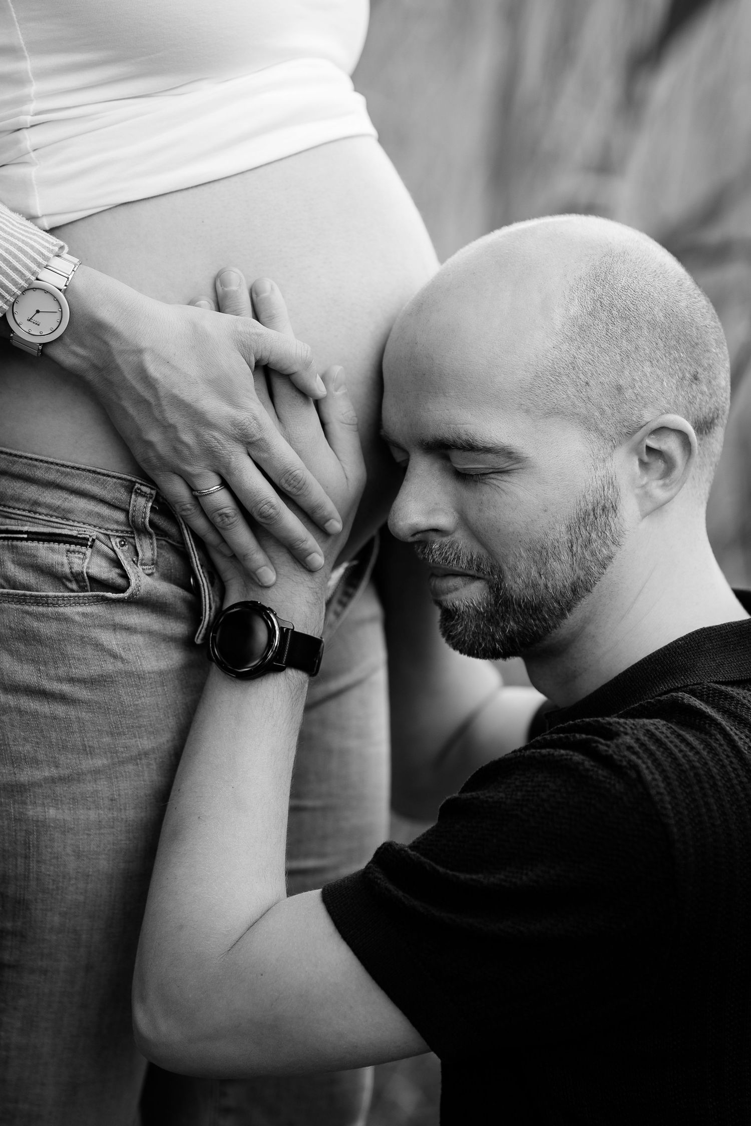 A tender black and white maternity photo showing an intimate moment with a pregnant belly.