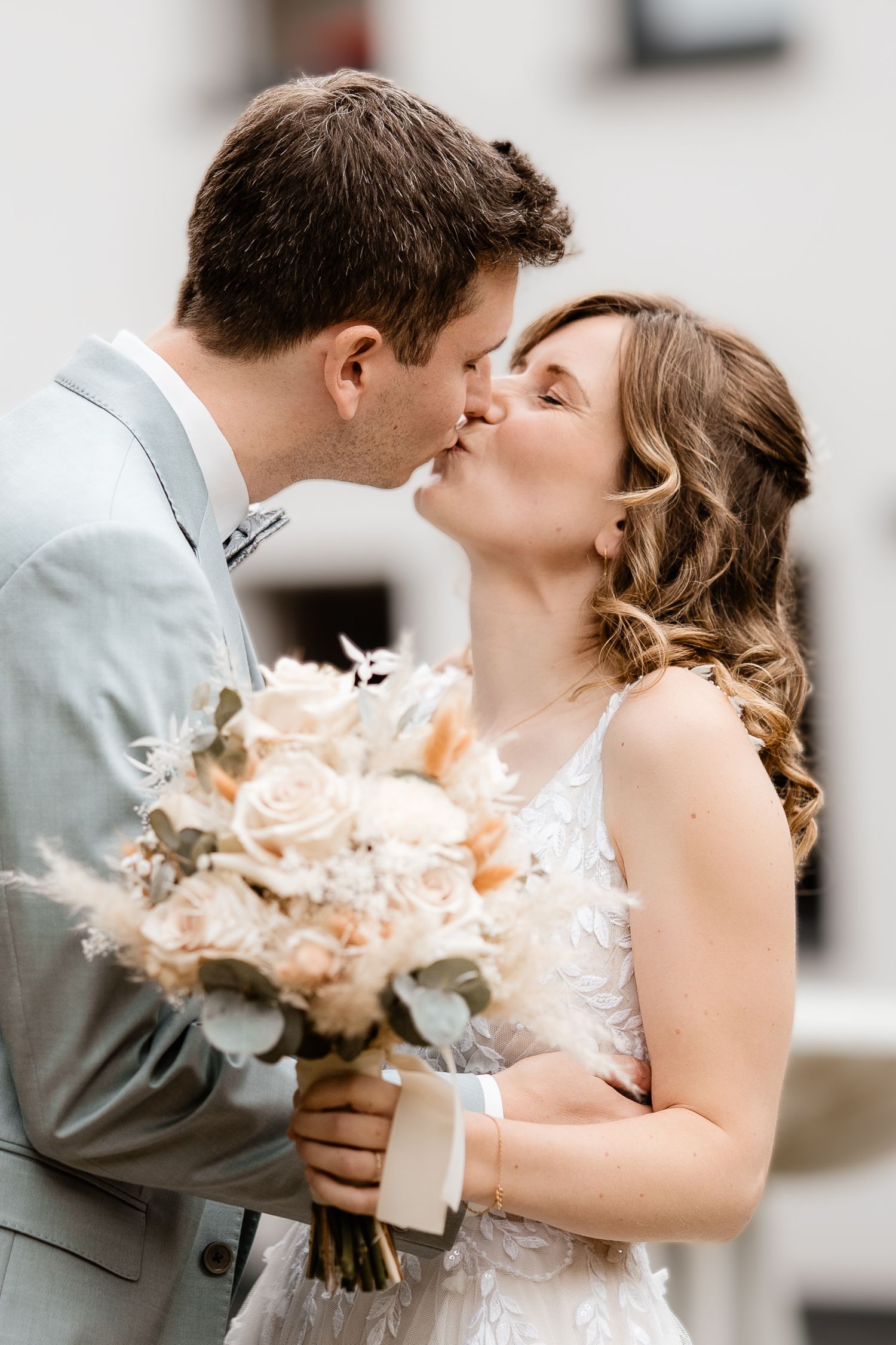 A bride and groom share a romantic kiss, she holds a bouquet of blush roses and eucalyptus on their wedding day.
