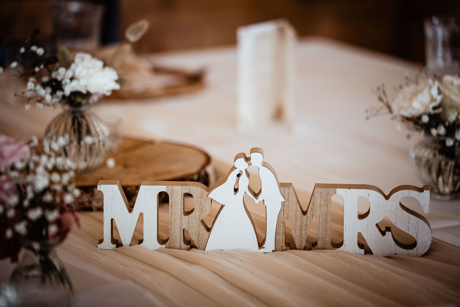 Wooden Mr & Mrs wedding sign with bride and groom silhouette on decorated table with floral arrangements.