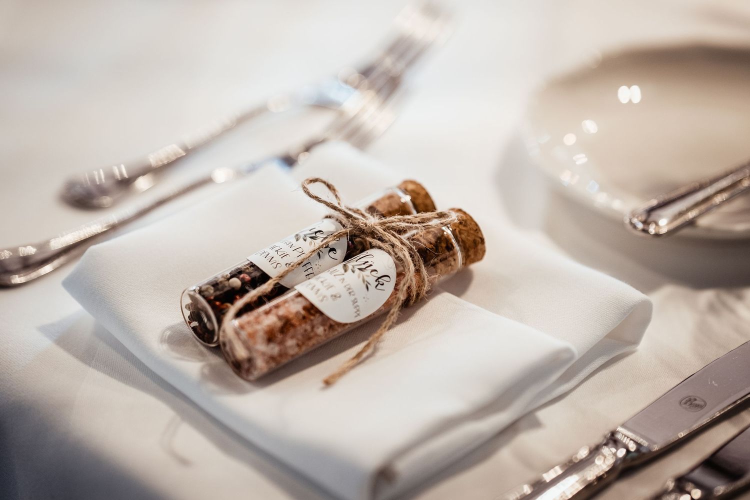 Elegant wedding favor with small bottles of salt and pepper tied with twine on napkin.