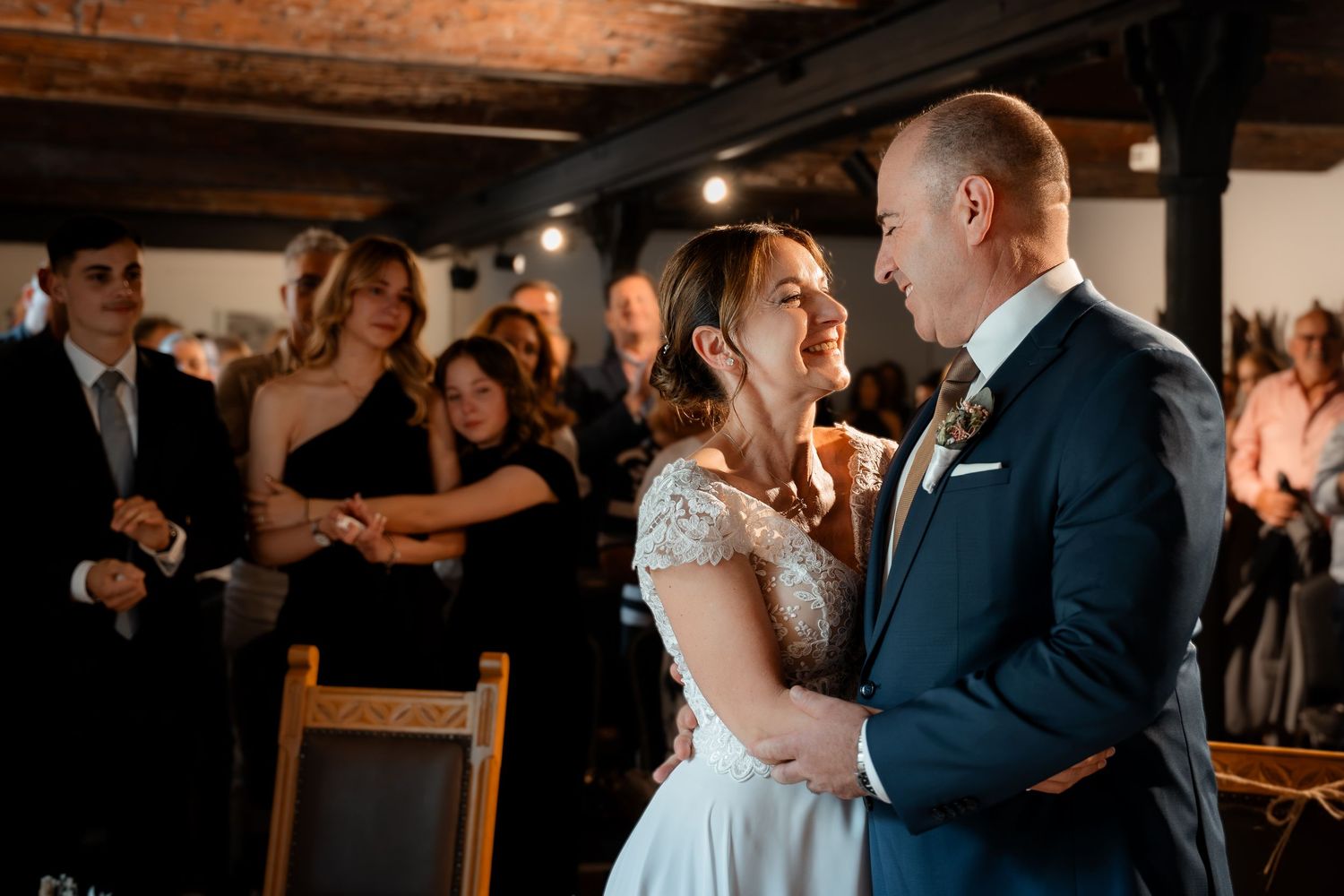Bride and groom share a tender moment during wedding ceremony with guests in background.