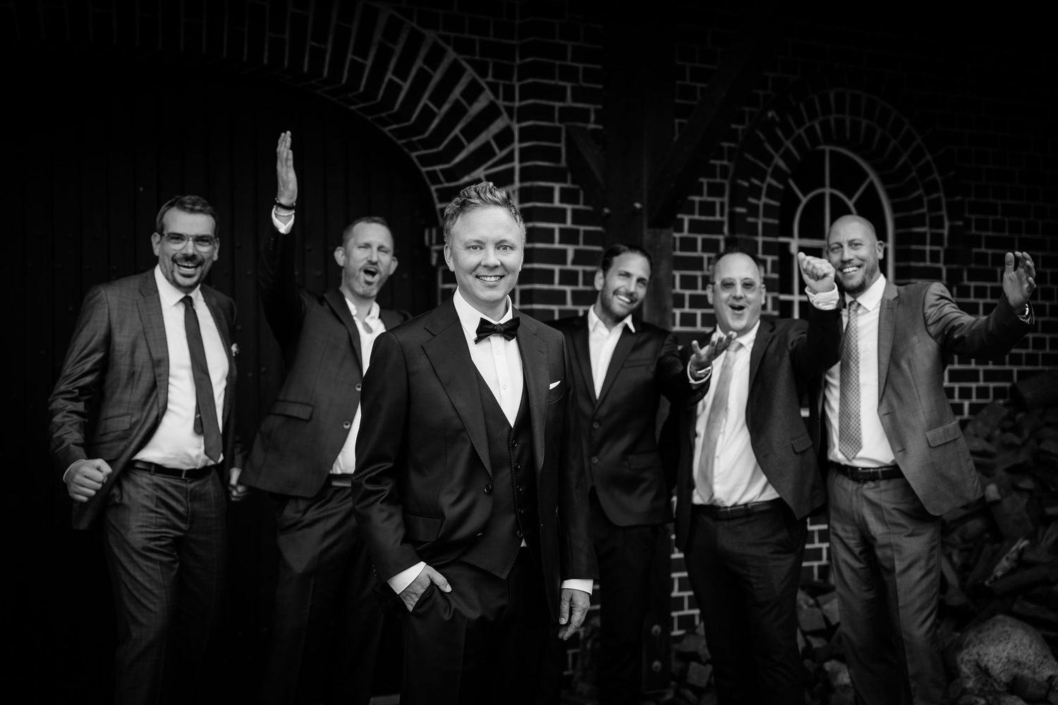 Black and white photo of groom in tuxedo celebrating with groomsmen in suits.