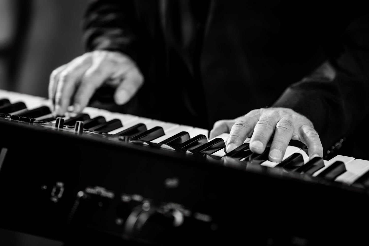 Close-up black and white photo of hands playing piano keys on a professional keyboard instrument.