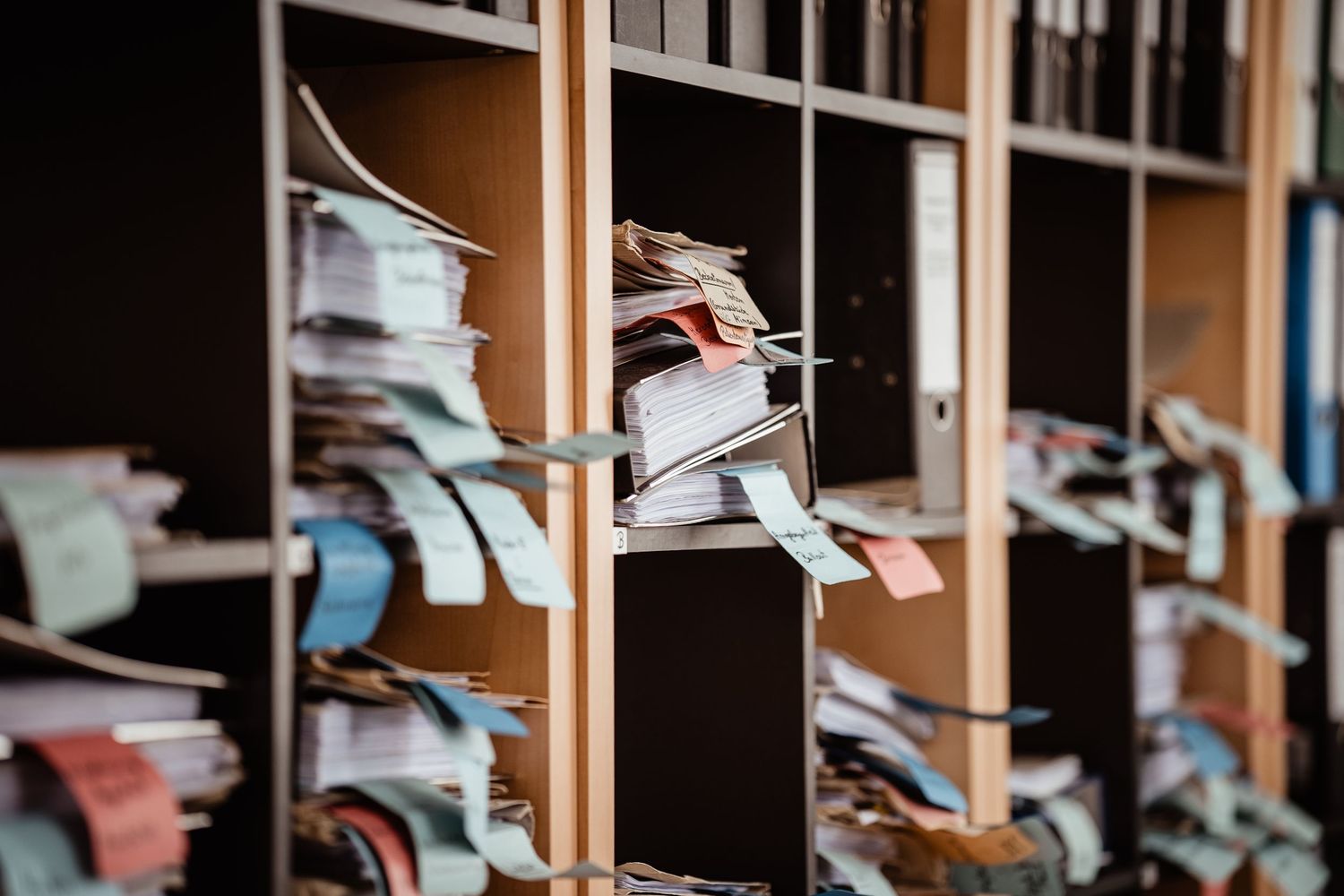 Wooden cubby shelving system filled with stacks of papers and documents.