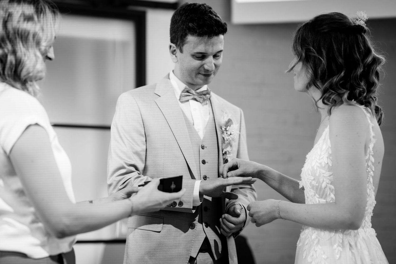 Black and white photo of bride placing ring on grooms finger during wedding ceremony.