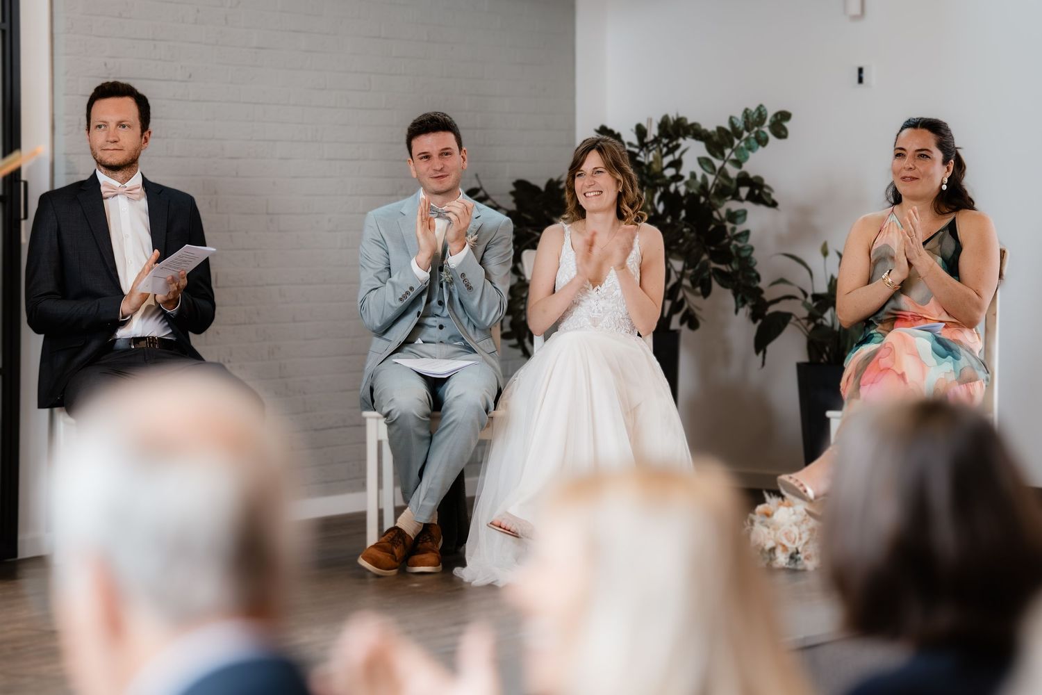 Wedding couple clapping with officiant and guest seated during an indoor wedding ceremony.